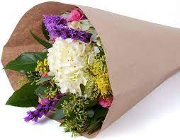 Hand-tied bouquet of white hydrangea with purple, yellow, and pink blooms wrapped in brown kraft paper.