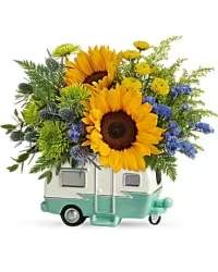 Sunshine &amp; Lavender Modern Arrangement - A contemporary and playful modern floral arrangement presented in a travel camper–style container. This vibrant design features a lively mix of sunflowers, yellow button mums, lavender statice, solidago, asters, green mums, leatherleaf, and Dynamite Eryngium, creating a unique combination of colors, textures, and height.  Perfect for brightening a space, gifting for celebrations, or adding a modern touch to décor, this arrangement blends cheerful yellow blooms with soft lavender and fresh greenery, offering a striking and memorable floral display.