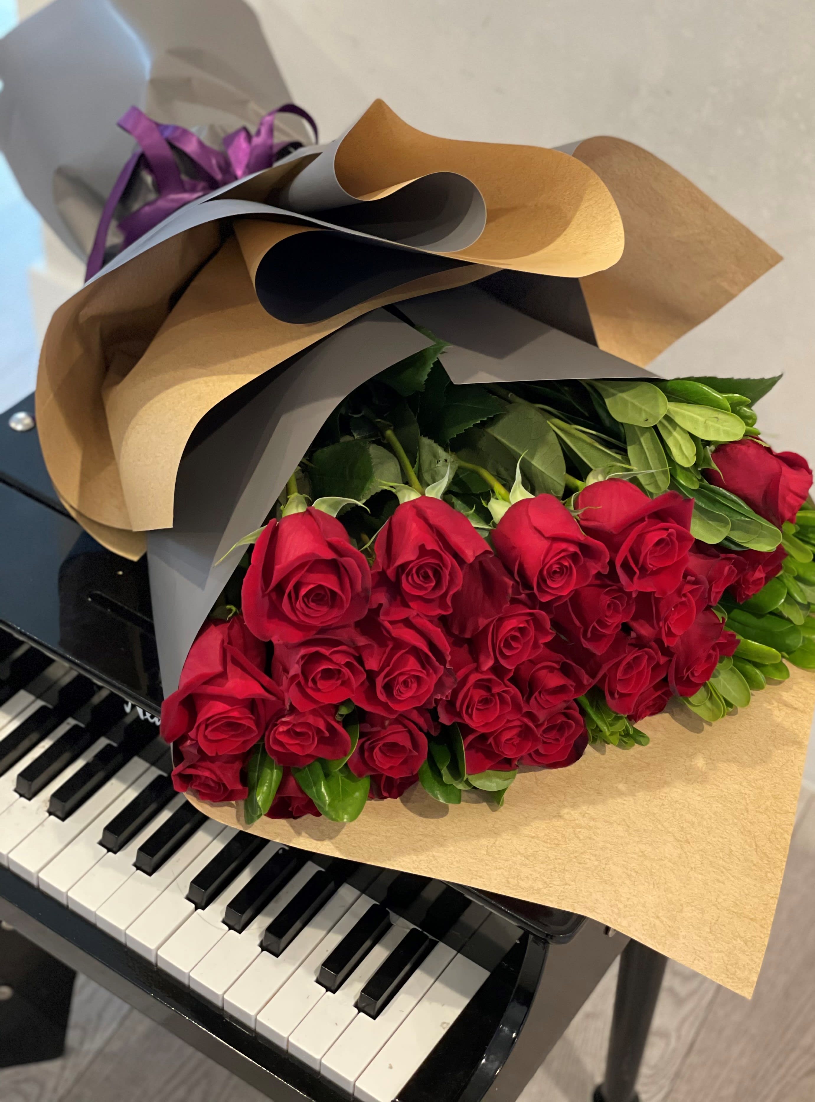 Bouquet of long-stem red roses wrapped in kraft paper resting on a black piano keyboard