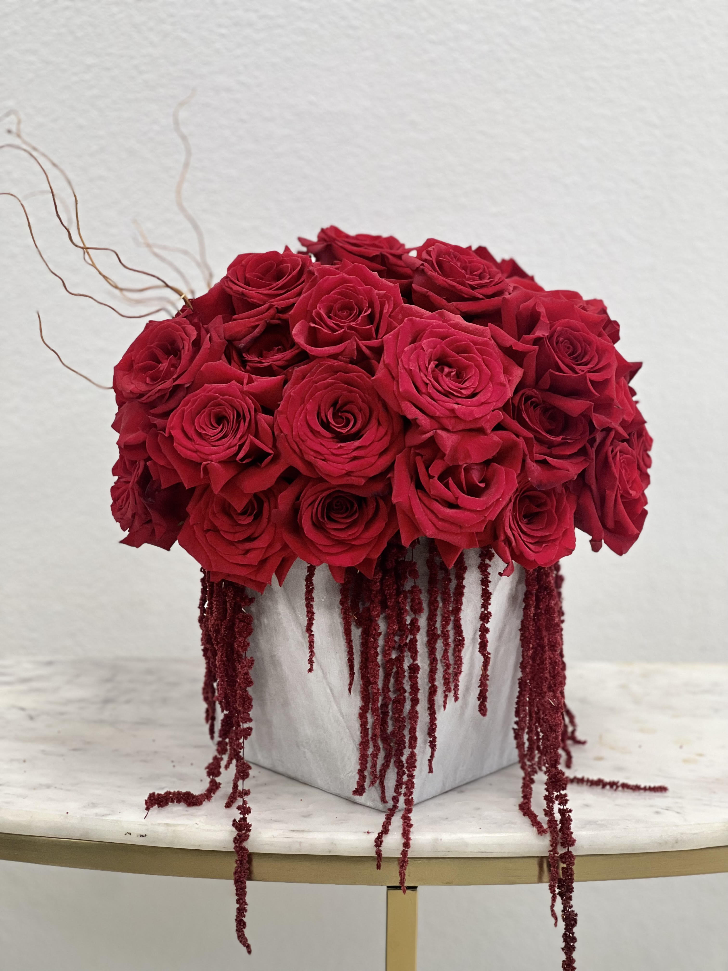 Compact arrangement of red roses with trailing red accents in a gray cube vase on a small table