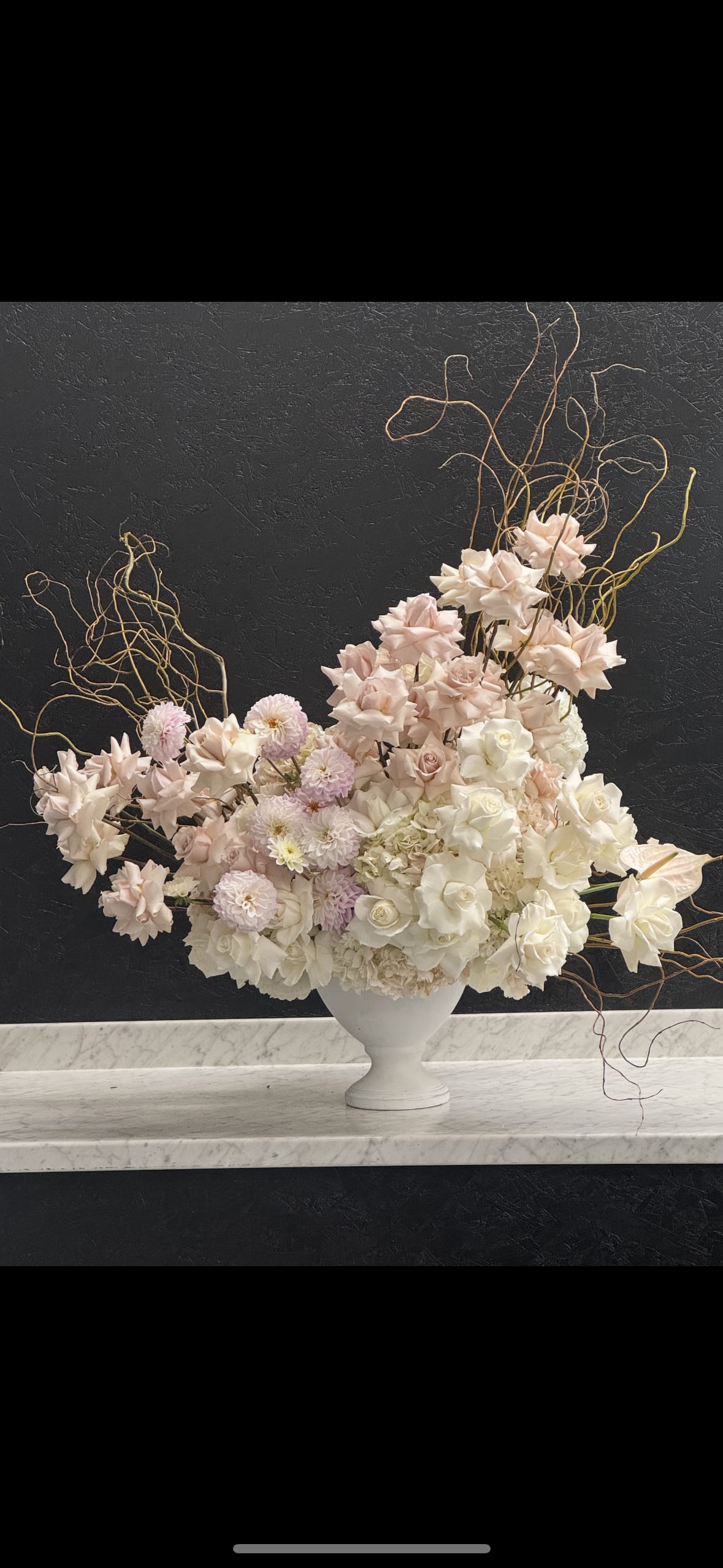 Large asymmetrical arrangement of blush and white flowers in a white urn