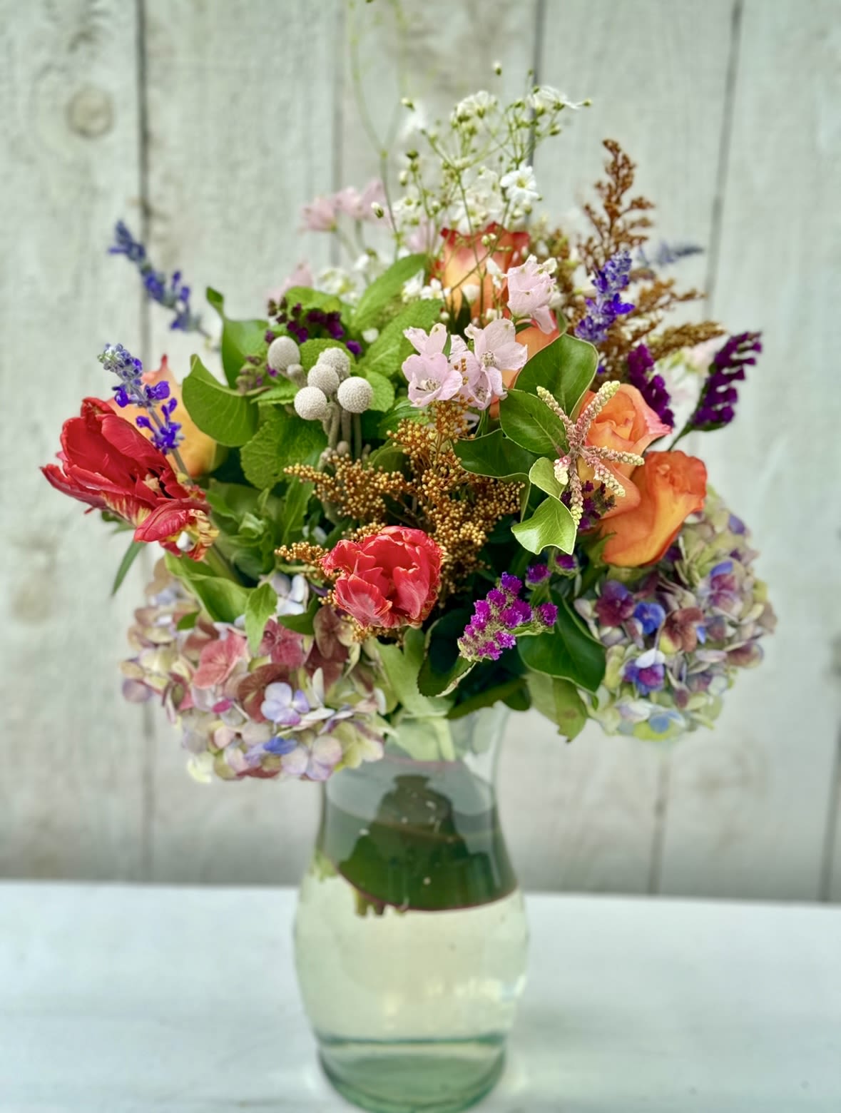 Mixed bouquet of colorful roses, tulips, and hydrangeas in a clear glass vase