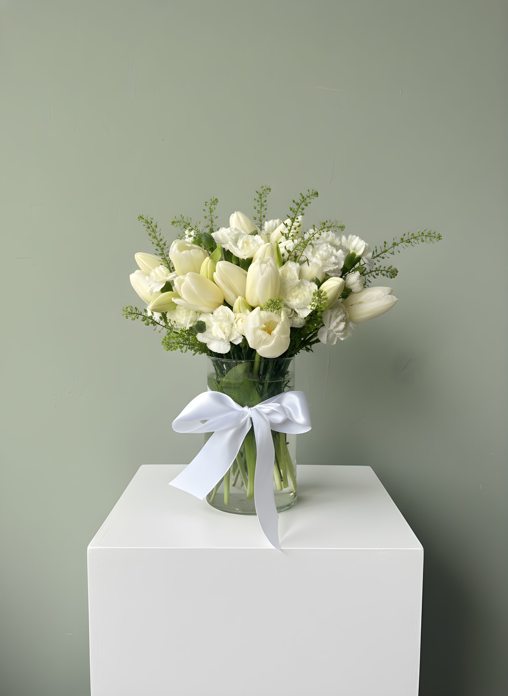 Pure White Tulip Elegance - A fresh and graceful arrangement showcasing the natural beauty of white tulips paired with delicate seasonal blooms and lush greenery. Designed in a clear glass vase and finished with a soft white ribbon, this arrangement brings a clean, airy, and elegant feel to any space.  Perfect for expressing sympathy, celebrating new beginnings, or sending a thoughtful and timeless gift.   Ideal for: • Sympathy &amp; condolences • New baby / new beginnings • Get well wishes • Everyday elegance  Please note: Tulips may arrive in a more closed form and will naturally open over time. Flower varieties may vary slightly based on availability while maintaining the same color palette, style, and fullness.