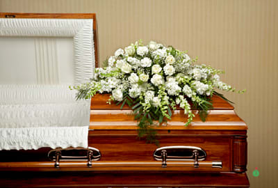 White floral casket spray arranged on a polished wood coffin
