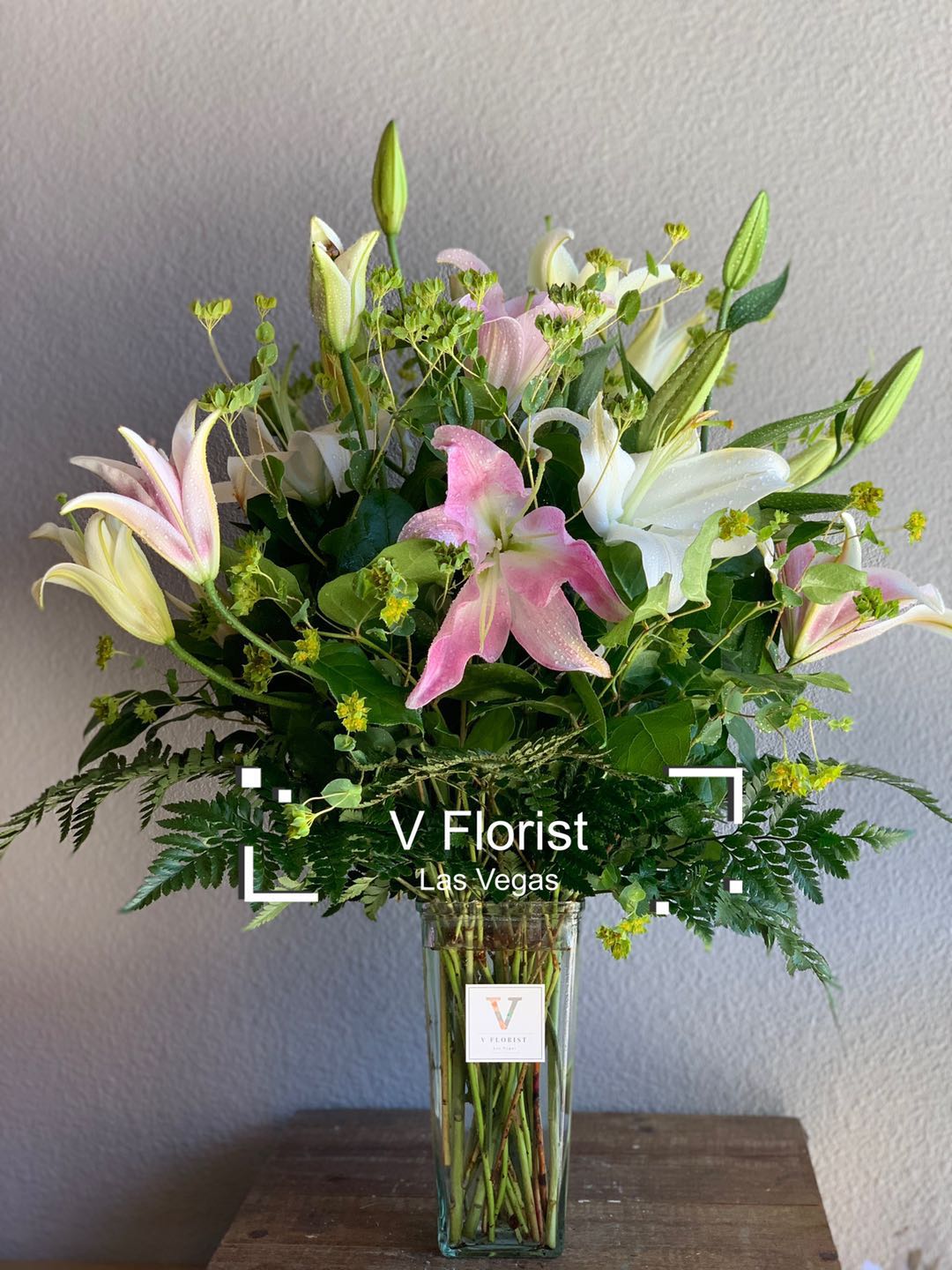 Tall arrangement of pink and white lilies with buds in a clear glass vase with ferns.