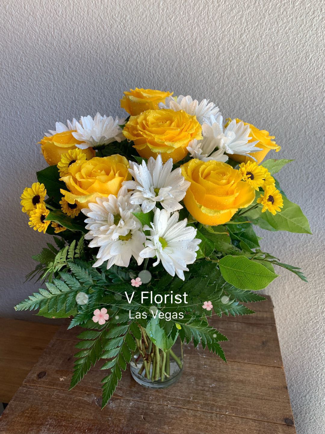 Arrangement of yellow roses and white daisies in a clear glass vase on a wooden surface