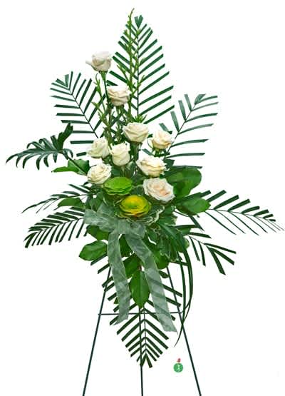 Tall standing spray of white roses with large palm fronds and green accents on an easel