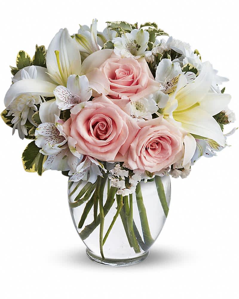 Round arrangement of pale pink roses and white lilies in a clear glass vase
