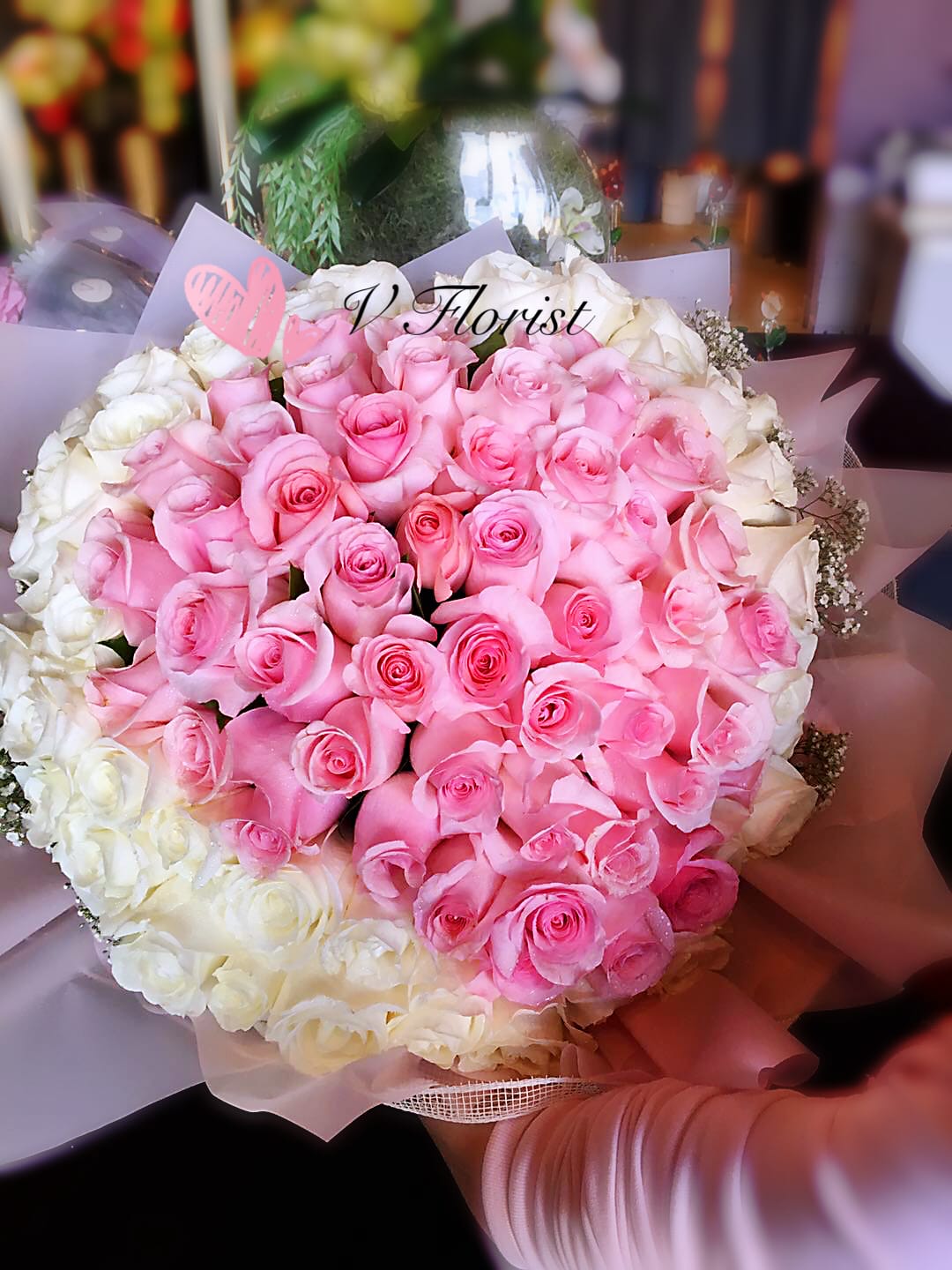 Large round bouquet of pink roses encircled by white roses in pastel wrapping paper