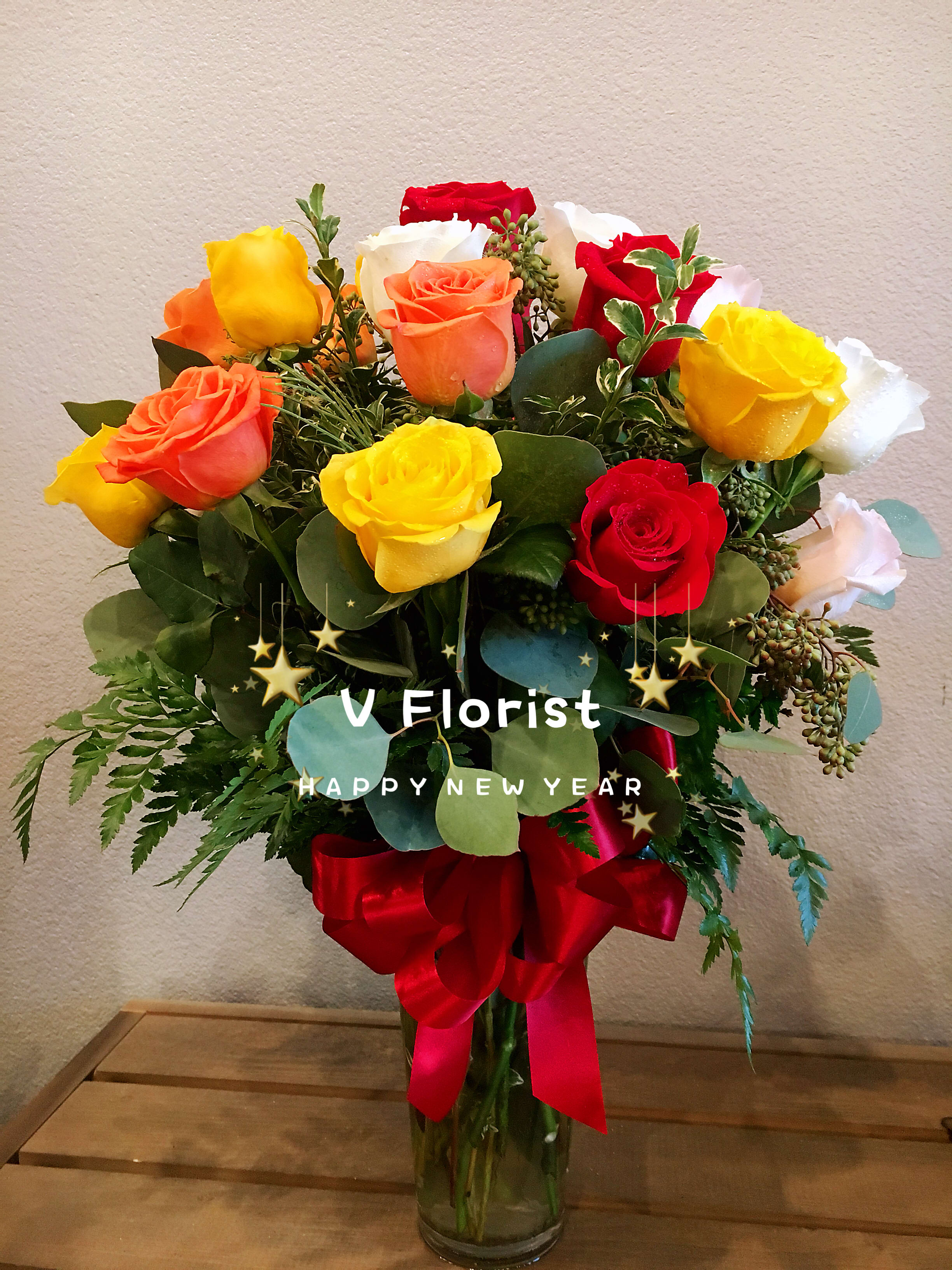 Tall glass vase of mixed red, yellow, orange, and white roses tied with a red bow