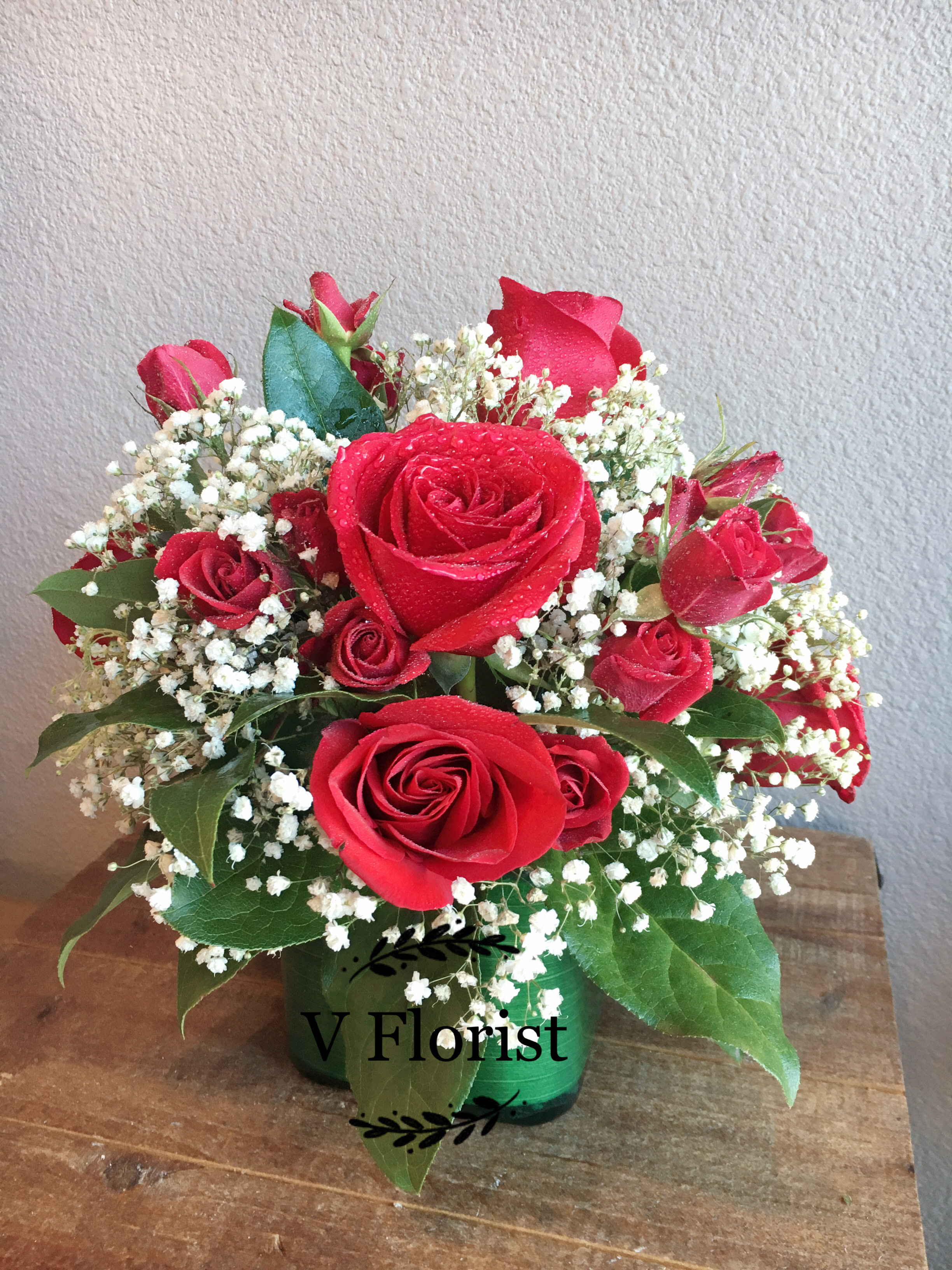 Compact arrangement of red roses and baby's breath in a green glass vase