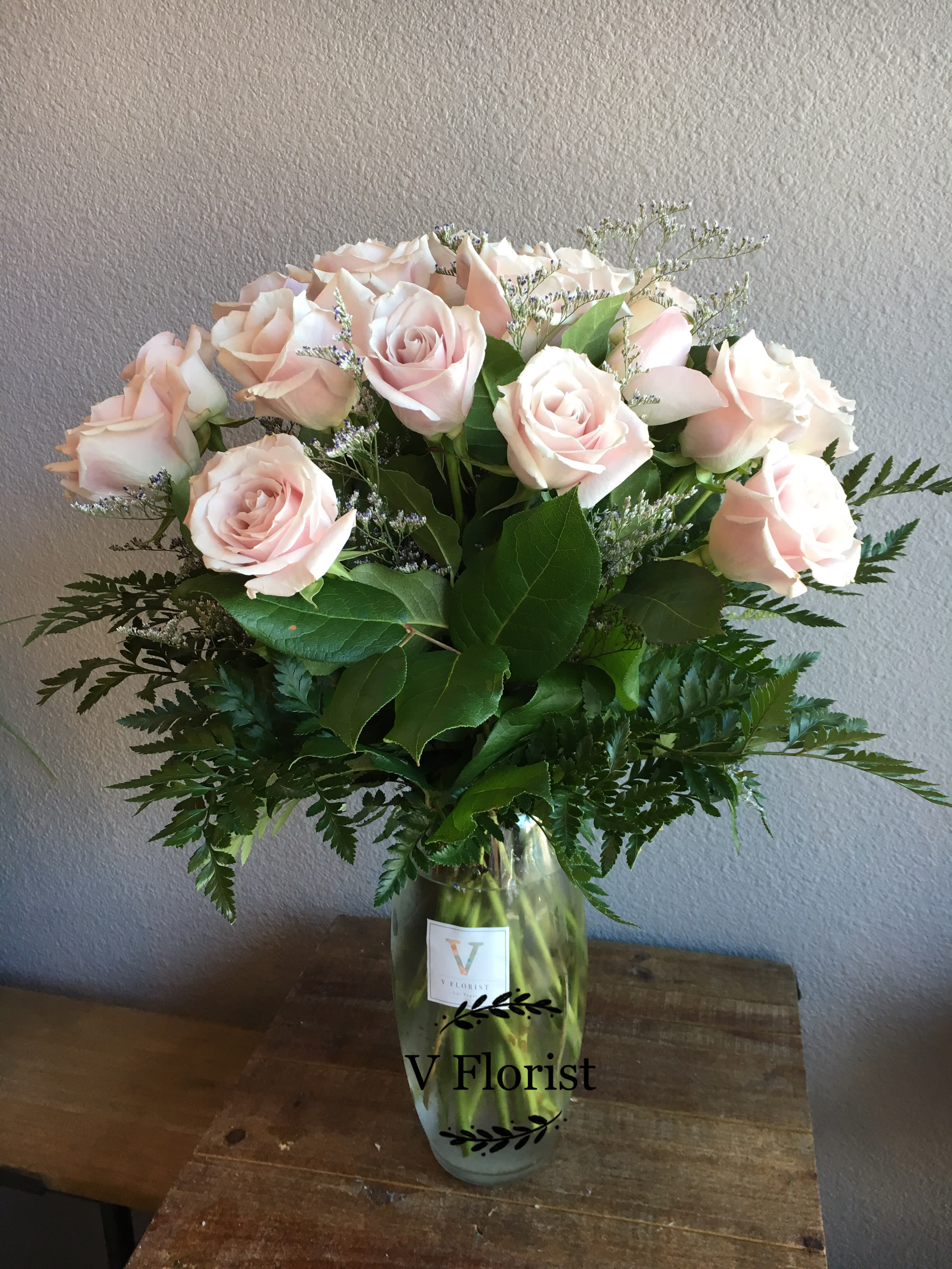 Tall vase arrangement of pale pink roses with white filler flowers.