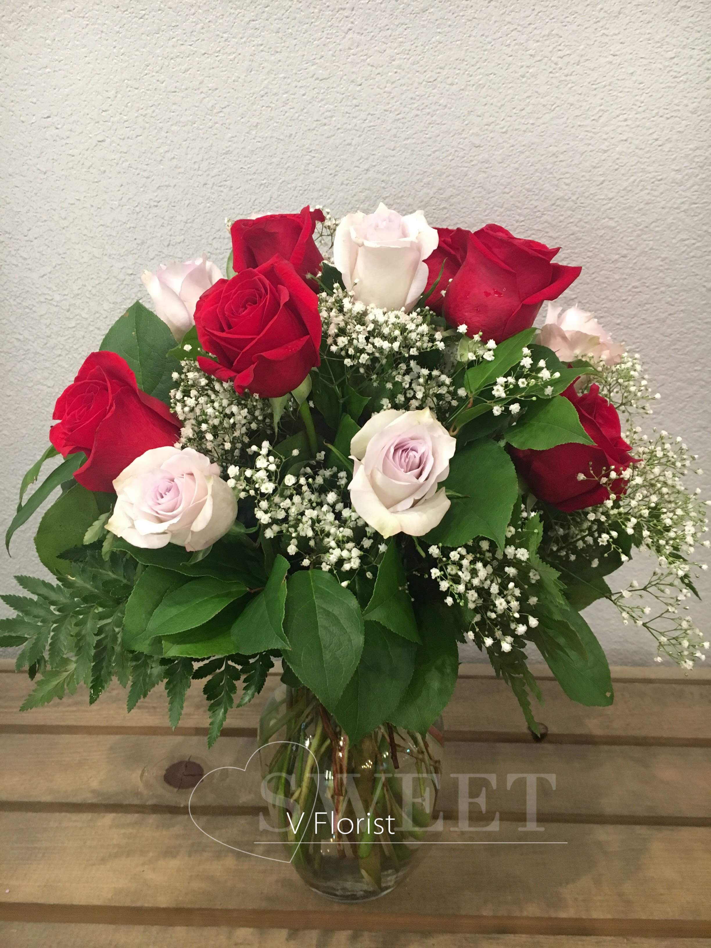Arrangement of red and pale pink roses with white filler flowers in a clear glass vase on a wooden surface