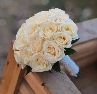 Pure Elegance - Pure Elegance is a timeless bridal bouquet composed of premium white roses arranged in a perfectly rounded, classic shape. This design embodies simplicity, purity, and refined sophistication, making it an ideal choice for a bride who appreciates traditional beauty and graceful style. Each rose is carefully selected for its fullness and softness, creating a lush, harmonious composition with a smooth, polished finish. The clean, structured form enhances the natural beauty of the flowers, allowing their elegance to speak without distraction. Finished with a neatly wrapped handle, this bouquet complements both classic and modern wedding gowns, adding a touch of understated luxury to your special day. Pure Elegance is designed to remain effortlessly beautiful in every moment — from ceremony to photographs and beyond.