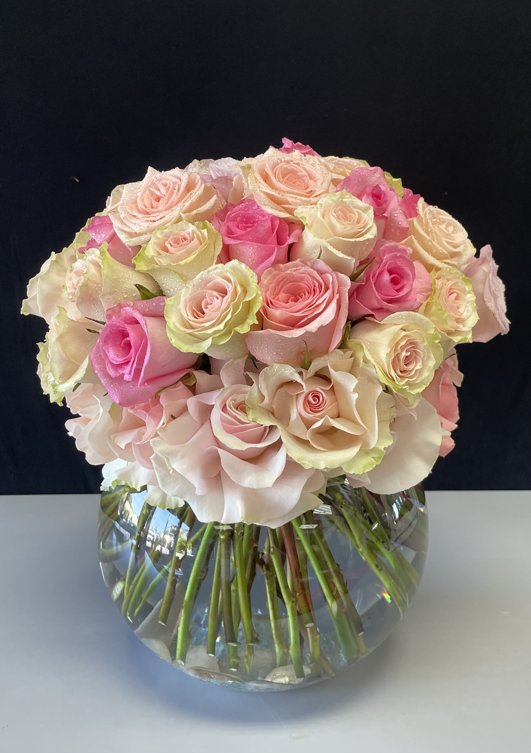 Whispering Blooms - A mix of light colored Roses, in pinks, peach and white. Arranged in a bubble bowl vase