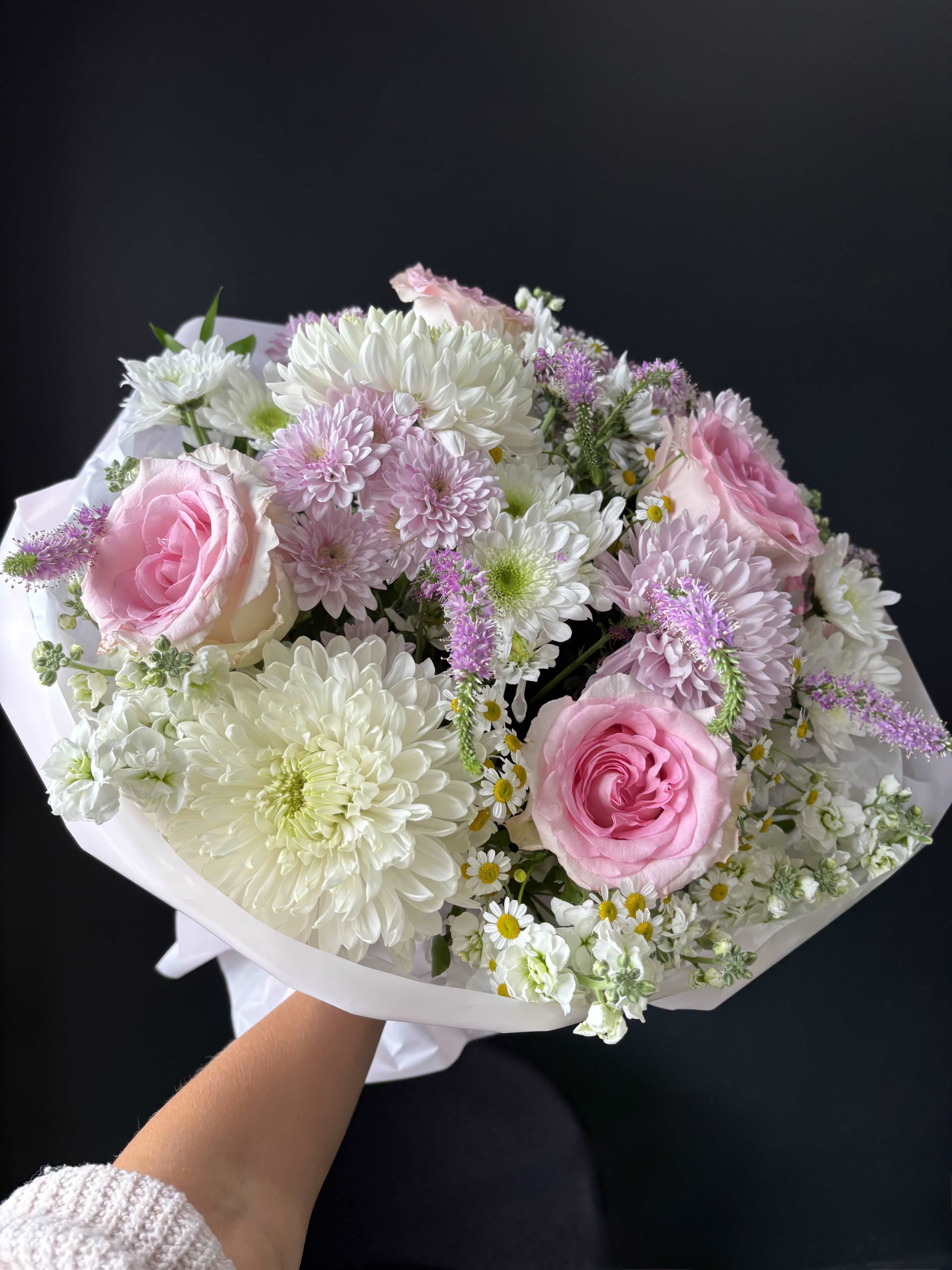 Soft Blush Garden - Soft Blush Garden is a delicate and airy bouquet inspired by the beauty of a blooming spring garden. Featuring soft pink roses, fluffy chrysanthemums, charming chamomile, and seasonal accents, this arrangement is designed with a natural, effortless flow. The gentle palette of blush, ivory, and soft lavender creates a calming and romantic feel, while the mix of textures adds depth and movement. Each bloom is thoughtfully placed to achieve a light yet full composition, balancing softness with refined elegance. Wrapped in clean, elegant paper, this bouquet feels fresh, feminine, and timeless — perfect for meaningful gifts, celebrations, or simply bringing a sense of beauty into everyday moments.