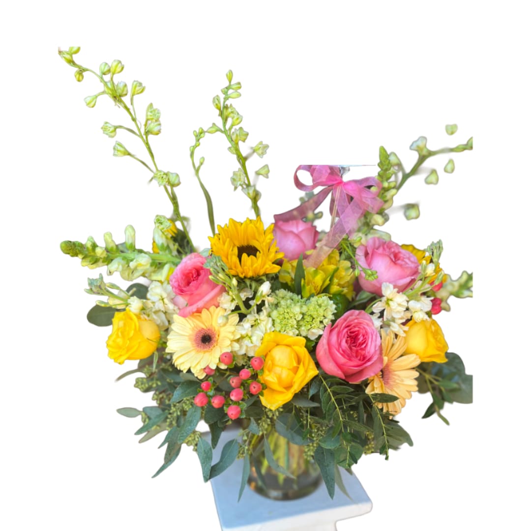 Spring Cottage - Bright, cheerful sunflowers and yellow roses mingle with pink roses and pale yellow gerbera daisies in this Spring Cottage flower arrangement-a perfect birthday bouquet, Mother's Day gift, or cheerful thinking-of-you surprise. Tall white and green snapdragons lift the composition while clustered green hydrangea and small red berries add texture, giving the recipient a lively, layered display that feels both celebratory and thoughtfully personal.  Arranged in a clear glass vase, the mix of yellow, pink, white, and green blooms creates a sunny palette that reads fresh and uplifting on any table or desk. Included hard goods- a printed card on a pick, a card holder pick, and a pink ribbon bow-make it ready to gift; the vase and floral height provide an eye-catching centerpiece without overwhelming a room.  This is the kind of bouquet that will make someone feel genuinely seen and celebrated-ideal for birthdays, congratulations, get well wishes, or just because. Standard care: keep flowers in fresh water, trim stems every few days, and place away from direct heat and sunlight to extend bloom life.