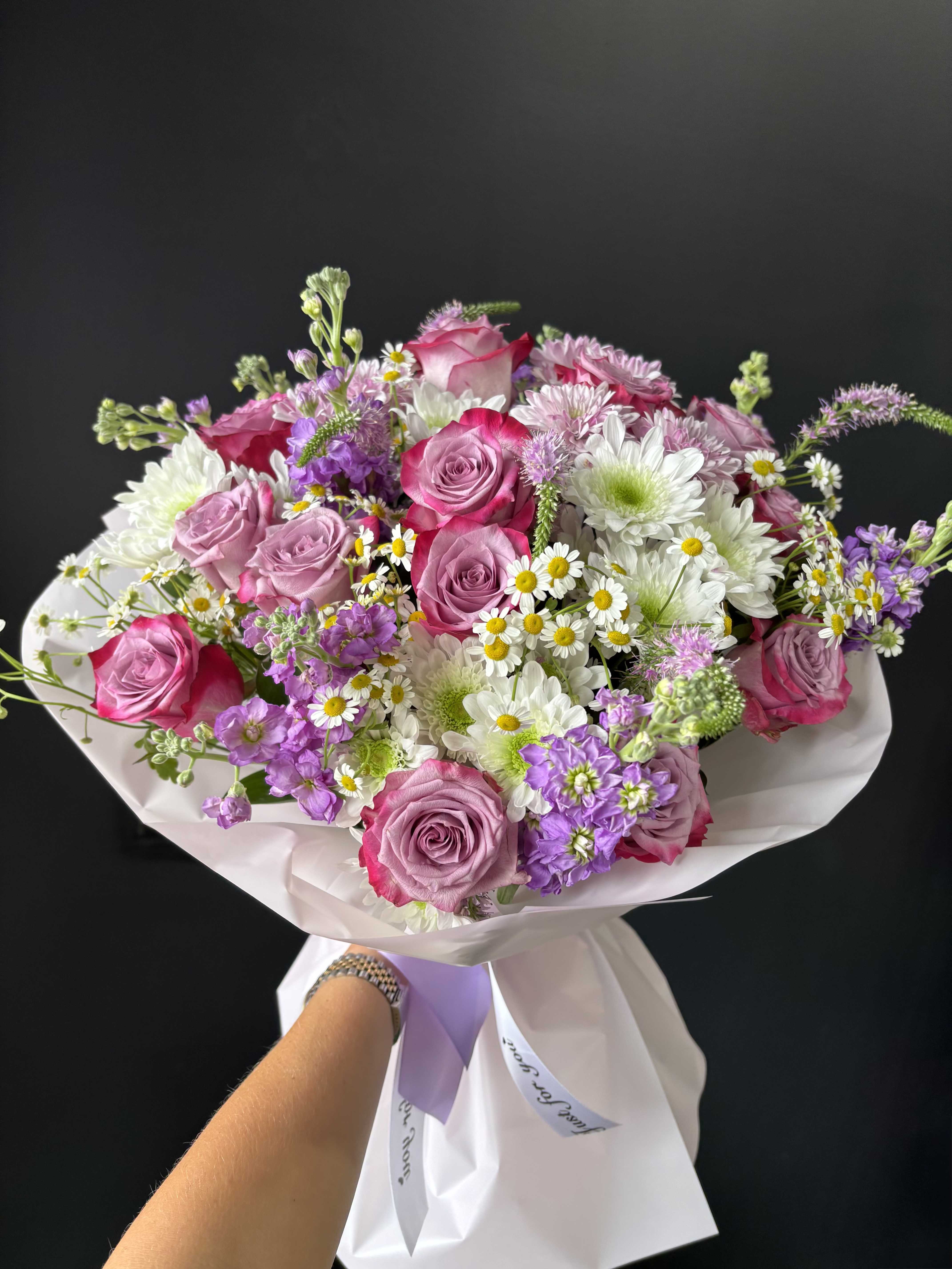 Lavender Blush Harmony - Lavender Blush Harmony is a soft, garden-inspired bouquet designed in a refined palette of blush pink, gentle lavender, and creamy white tones. Featuring elegant roses, airy chrysanthemums, delicate chamomile, and seasonal blooms, this arrangement captures a natural, effortless beauty with a polished and modern finish. Lavender accents bring a subtle depth and sophistication, elevating the bouquet beyond traditional pink tones. The composition is thoughtfully arranged to feel light and airy, yet full and balanced, with soft movement and layered textures. Wrapped in clean, elegant paper with delicate ribbon detailing, this bouquet feels fresh, feminine, and quietly luxurious — perfect for meaningful gifts, celebrations, or refined everyday moments.