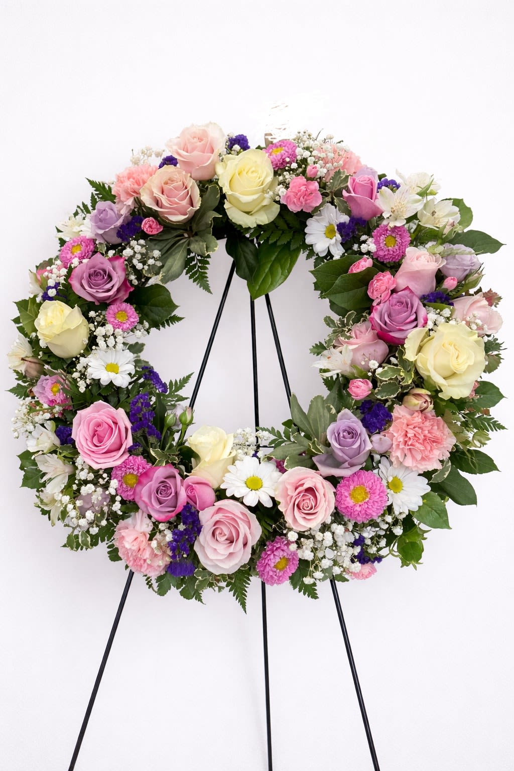 Pastel wreath of roses, daisies, carnations and filler flowers on a black easel stand