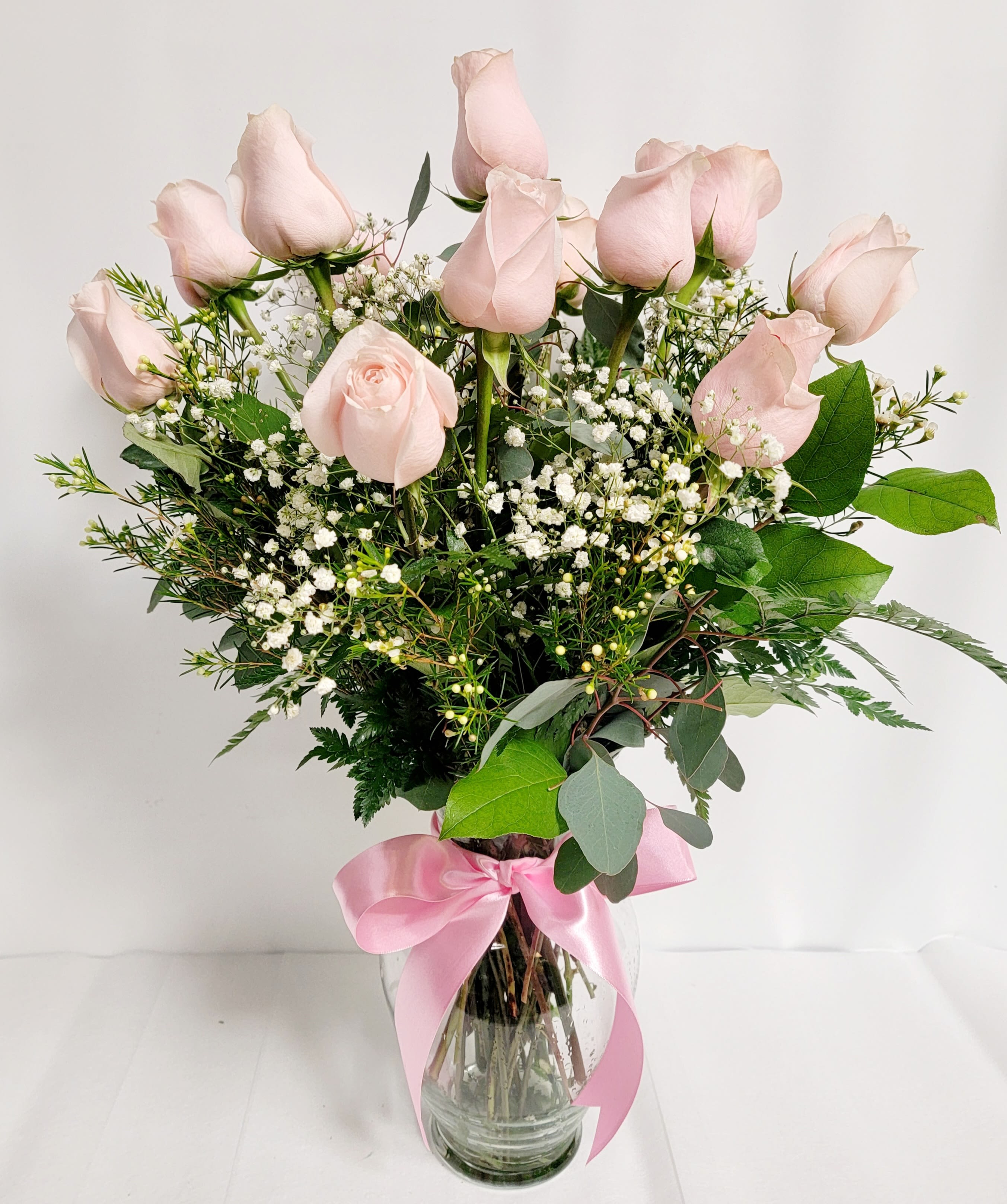Pink roses in a glass vase with baby's breath and a pink ribbon