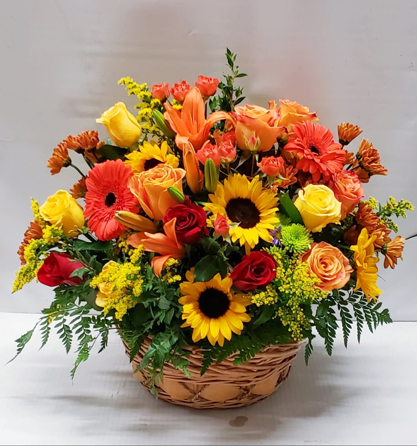 Mixed bouquet of roses, lilies, sunflowers, and gerbera daisies in a wicker basket