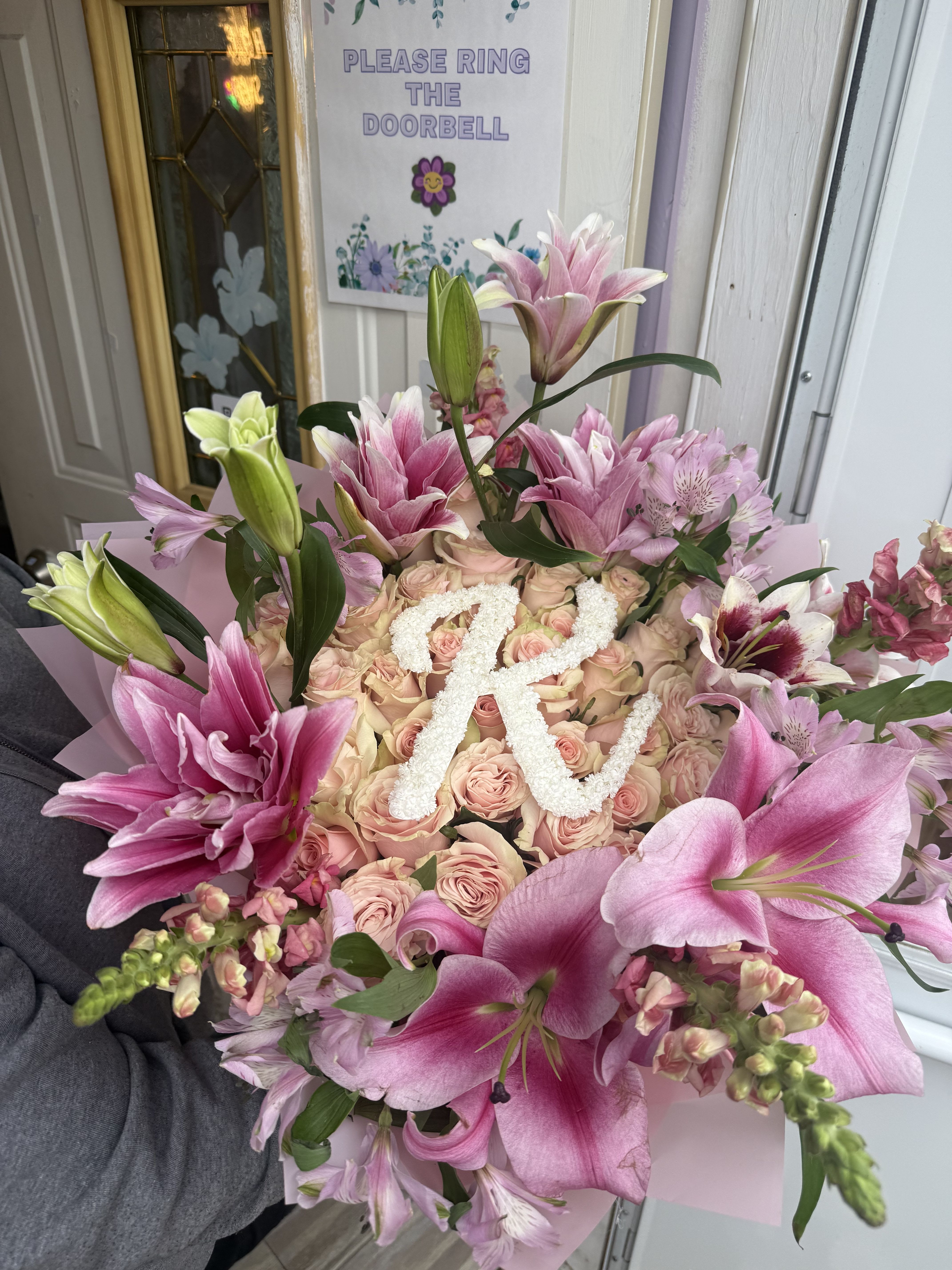 Pink lilies and roses arranged around a white floral letter R.