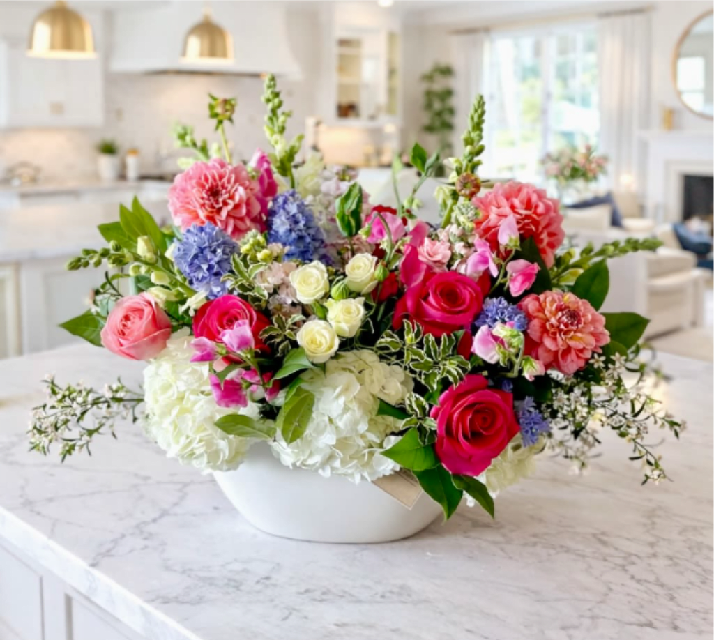 Mixed bouquet of pink, white, blue, and coral flowers in a white bowl vase