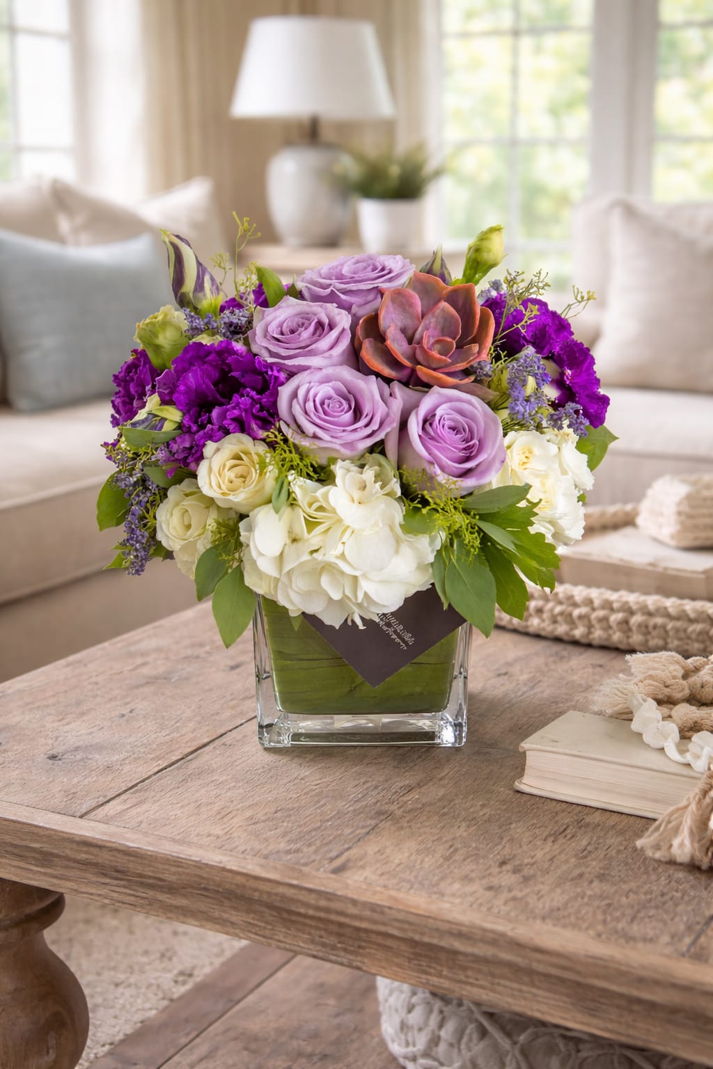 Janelle - 4X4 glass cube arrangement.  Introduce someone special to the timeless beauty of the Janelle arrangement. Elegance and sophistication abound in this delightful mix of lavender, purple, and white florals, with a delicate succulent that can be replanted for lasting enjoyment. Perfect as a memorable gift for any occasion, the Janelle radiates with its unique style and is perfect for family or friends who appreciate natural beauty in its finest form. With its lush texture and inviting design, the Janelle expresses sophisticated charm that will stand out in any setting. Let this one-of-a-kind arrangement bring elegance into your home or office space today!