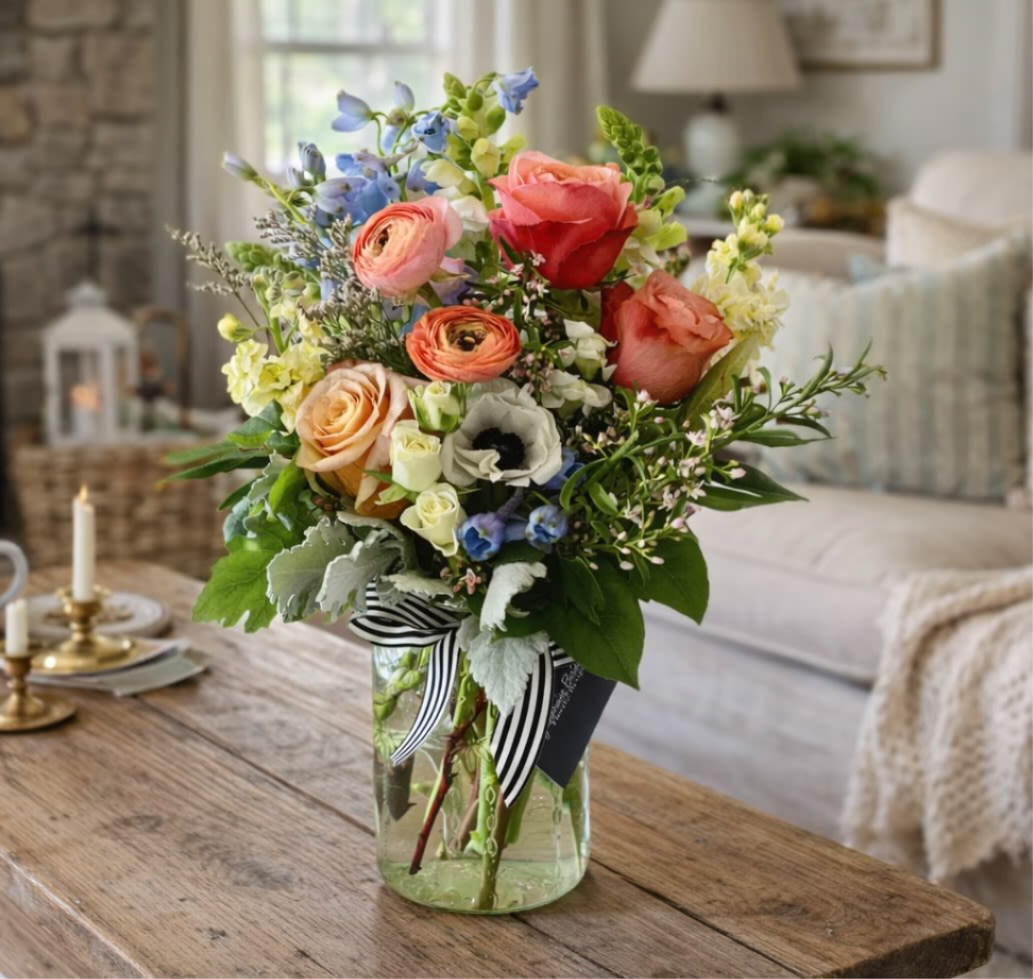 Mixed bouquet of roses, ranunculus, and blue flowers in a glass vase