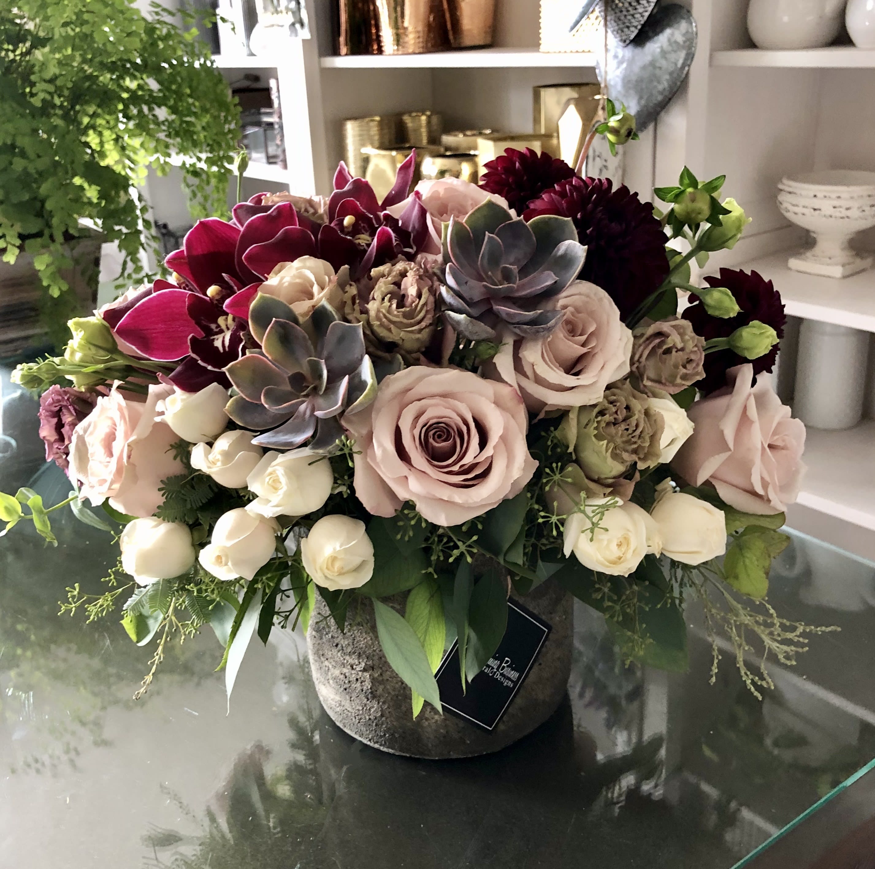 Mixed bouquet with pale roses, dark orchids, and succulents in a stone vase