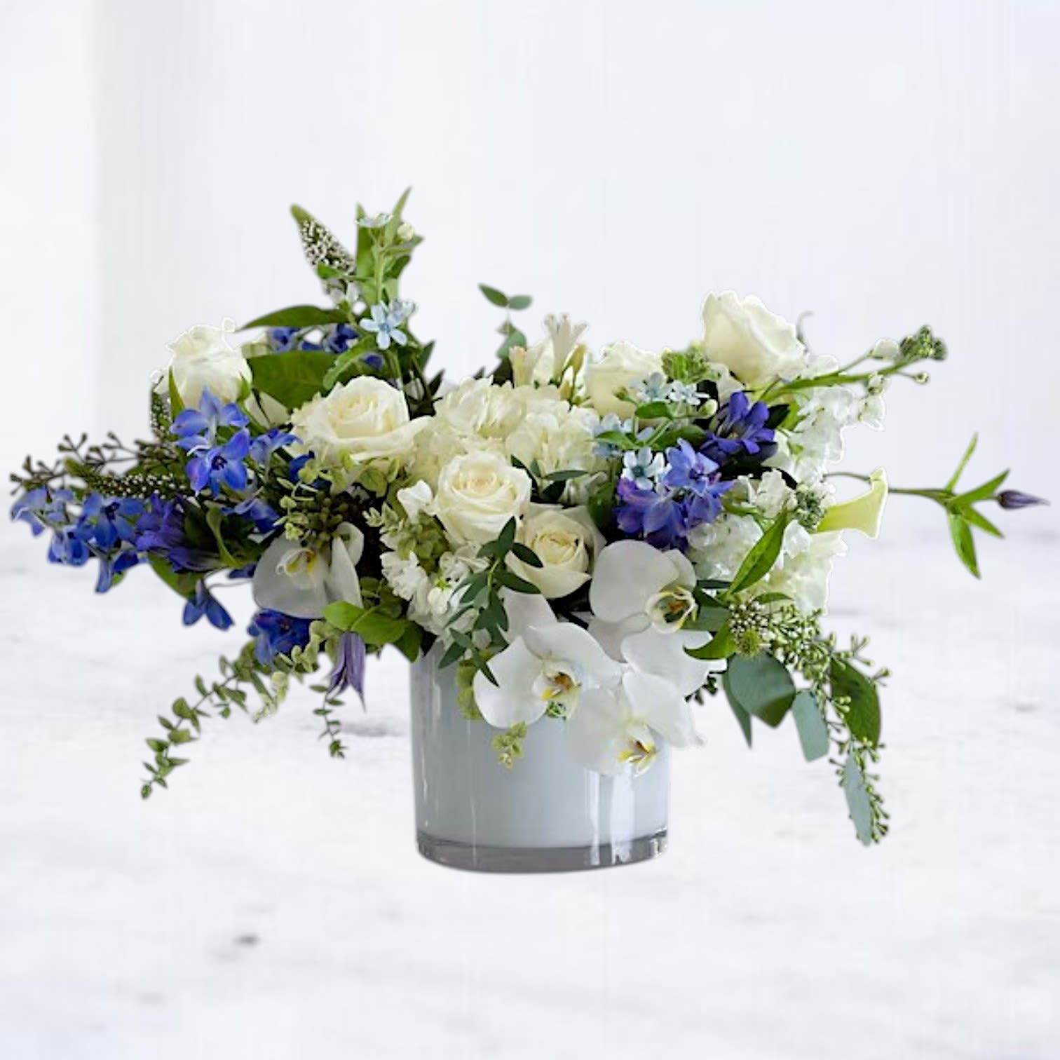 Liora - Timeless and sophisticated, a palette of vivid blue and soft white flowers including include roses, hydrangea, stock, delphinium, veronica and thistle, radiate refreshing beauty and bliss. Delicate greenery and a sleek white glass vase complete this classic look and make this popular design a versatile and naturally elegant addition to any room or occasion.  Whiskey Wallflower is a design-forward florist based in Magnolia, offering same-day flower delivery throughout Magnolia, Montgomery, The Woodlands, Conroe, Tomball, Willis, Spring, and surrounding North Houston communities. Each arrangement is thoughtfully composed using premium blooms, with a focus on modern design, quality, and intentional detail.