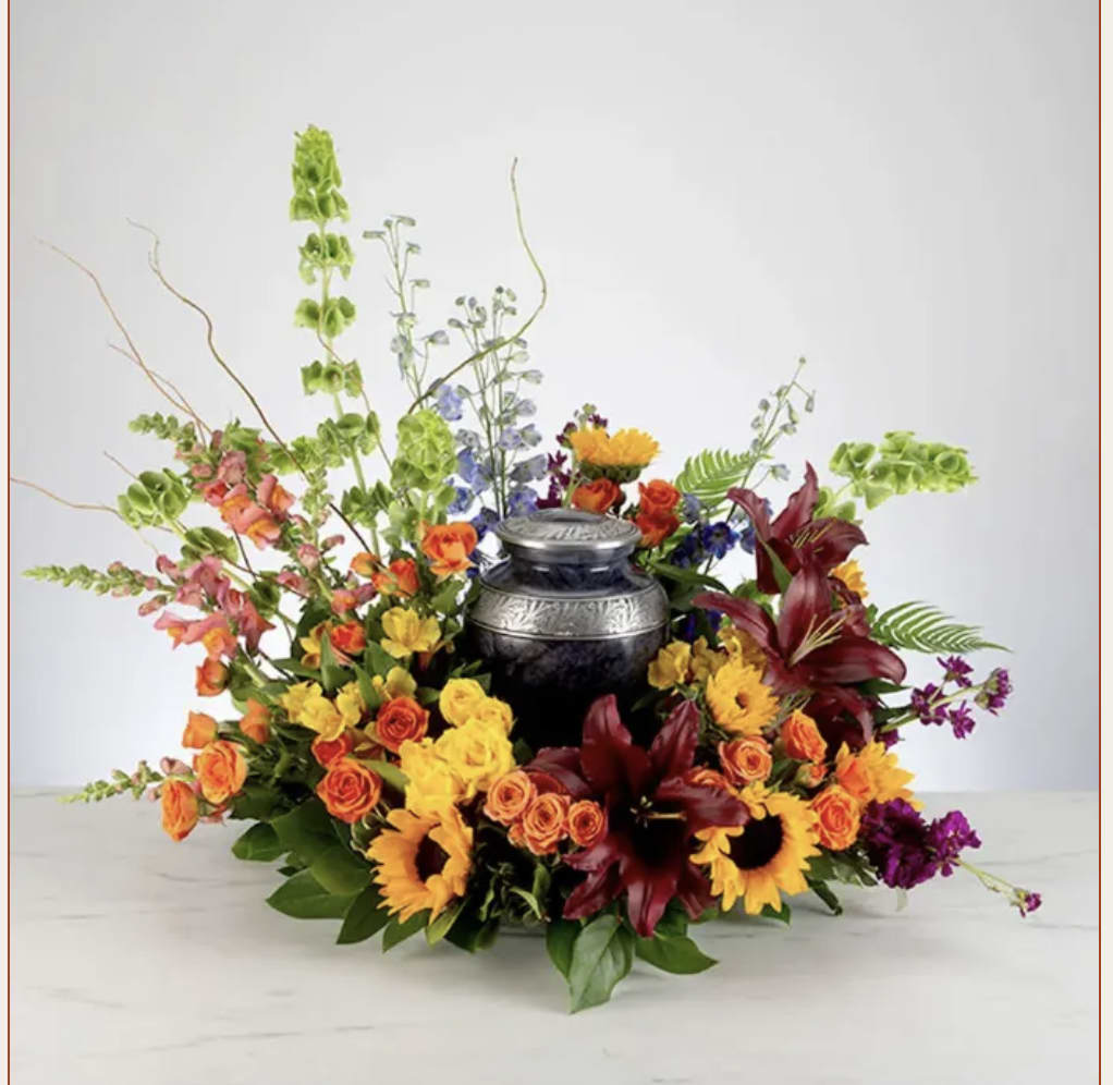 Colorful floral arrangement around a black urn with orange, yellow, and burgundy blooms