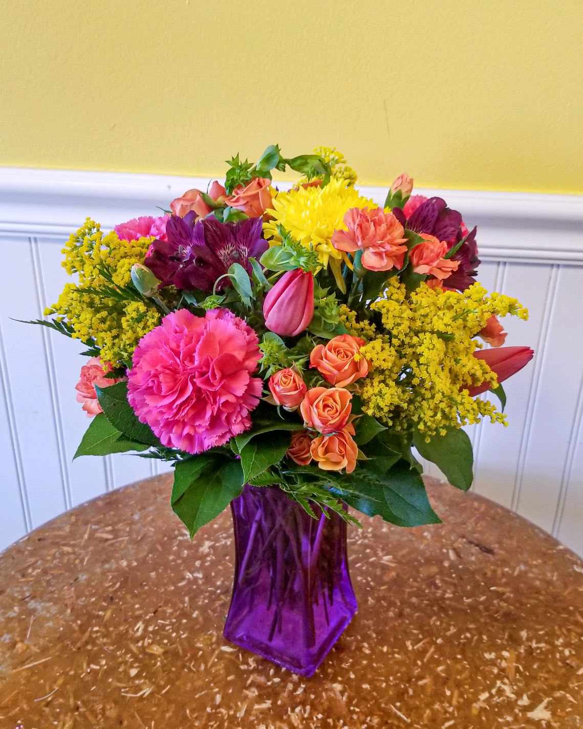 Spring Fields - Bright and vibrant blooms designed in a purple 8 inch vase. Approx dimensions 18in x 13in