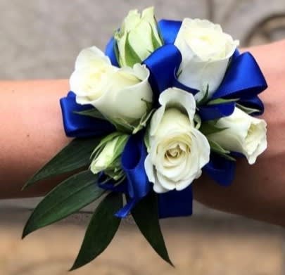 White rose wrist corsage with blue ribbon and green leaves
