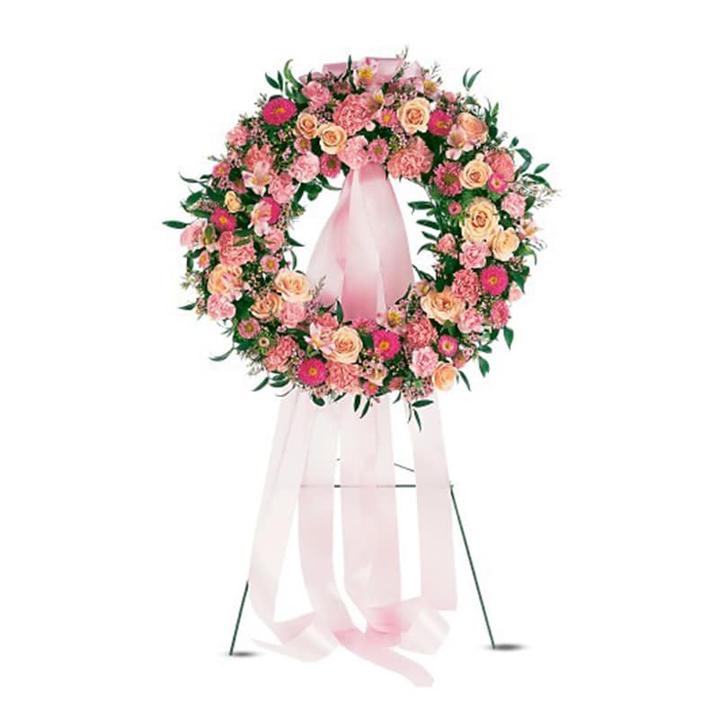 Pink and peach floral standing wreath with long pink ribbons on a metal easel