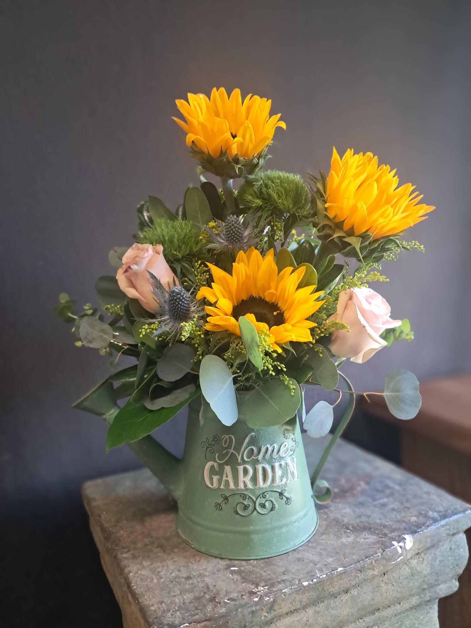 Sunny Rose Garden - Bring the charm of a cottage garden indoors with our Sunny Rose Garden watering can arrangement, featuring cheerful fresh sunflowers, soft light pink roses, and lush mixed greenery artfully designed in a green garden metal watering can vase.  The reusable green metal watering can doubles as a charming home décor piece or garden accessory.  Order this sunflower and pink rose watering can arrangement for same-day local flower delivery and send a little sunshine to someone special.