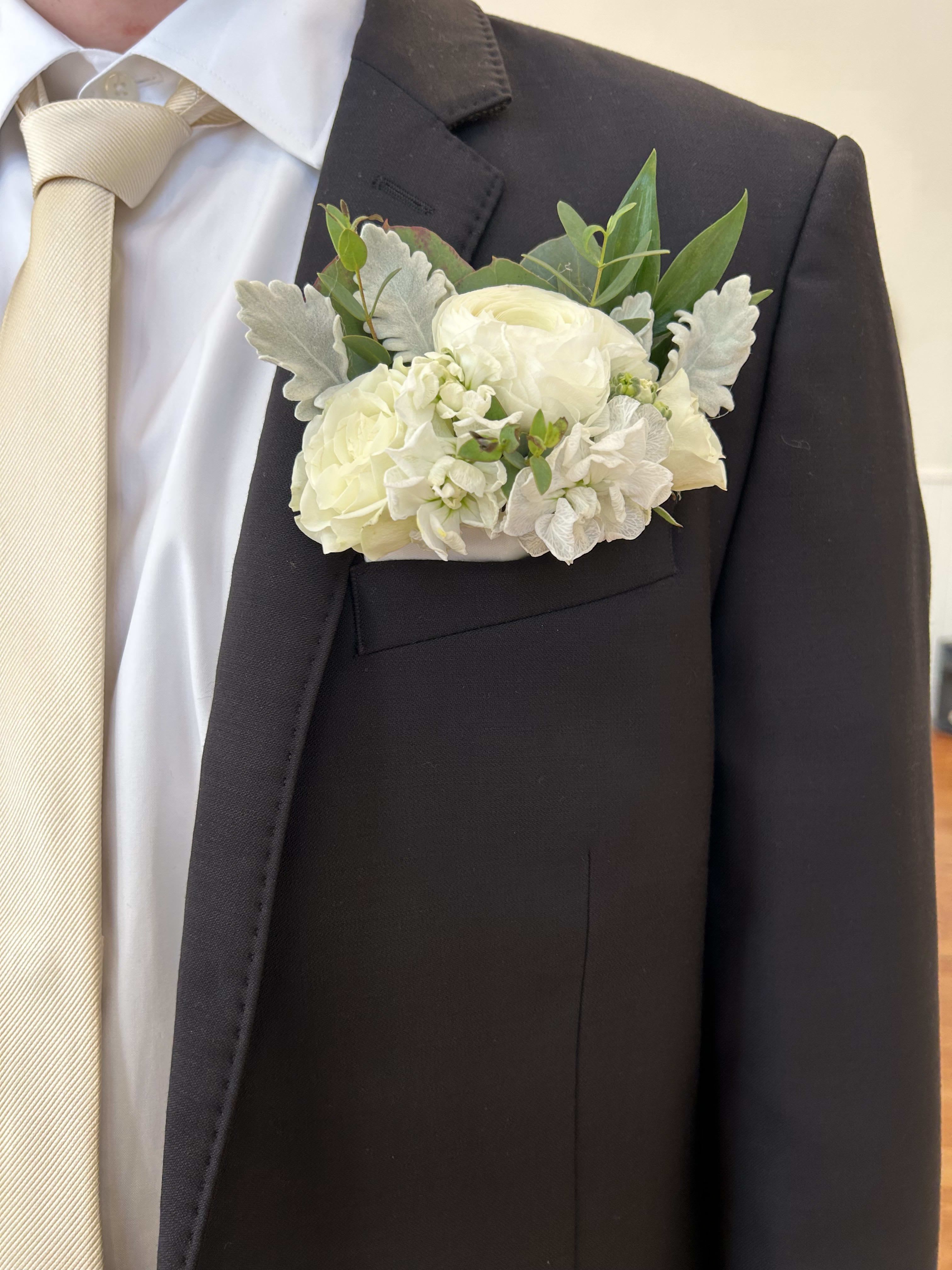 White boutonniere on a dark suit jacket with a cream tie