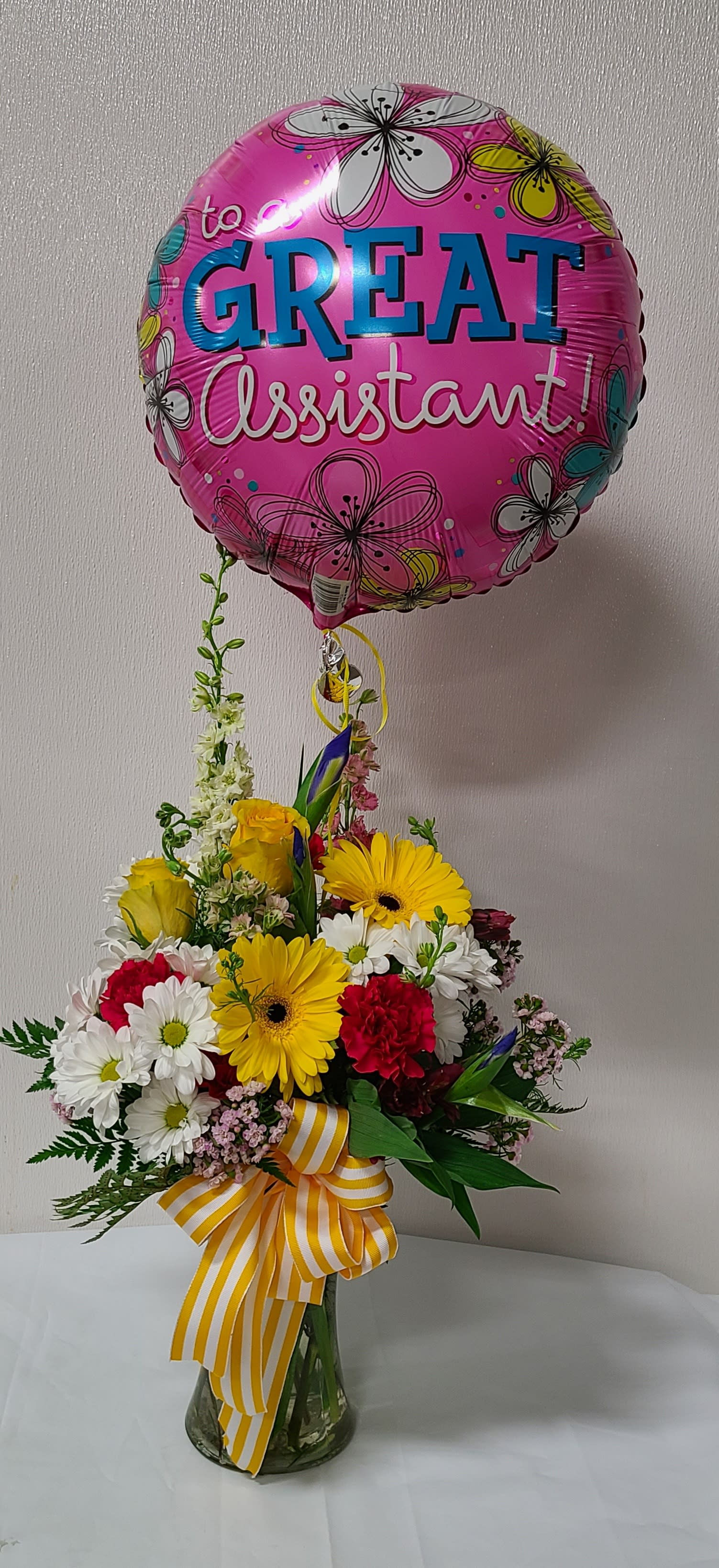Bouquet in a glass vase with a pink balloon reading "Great Assistant!"