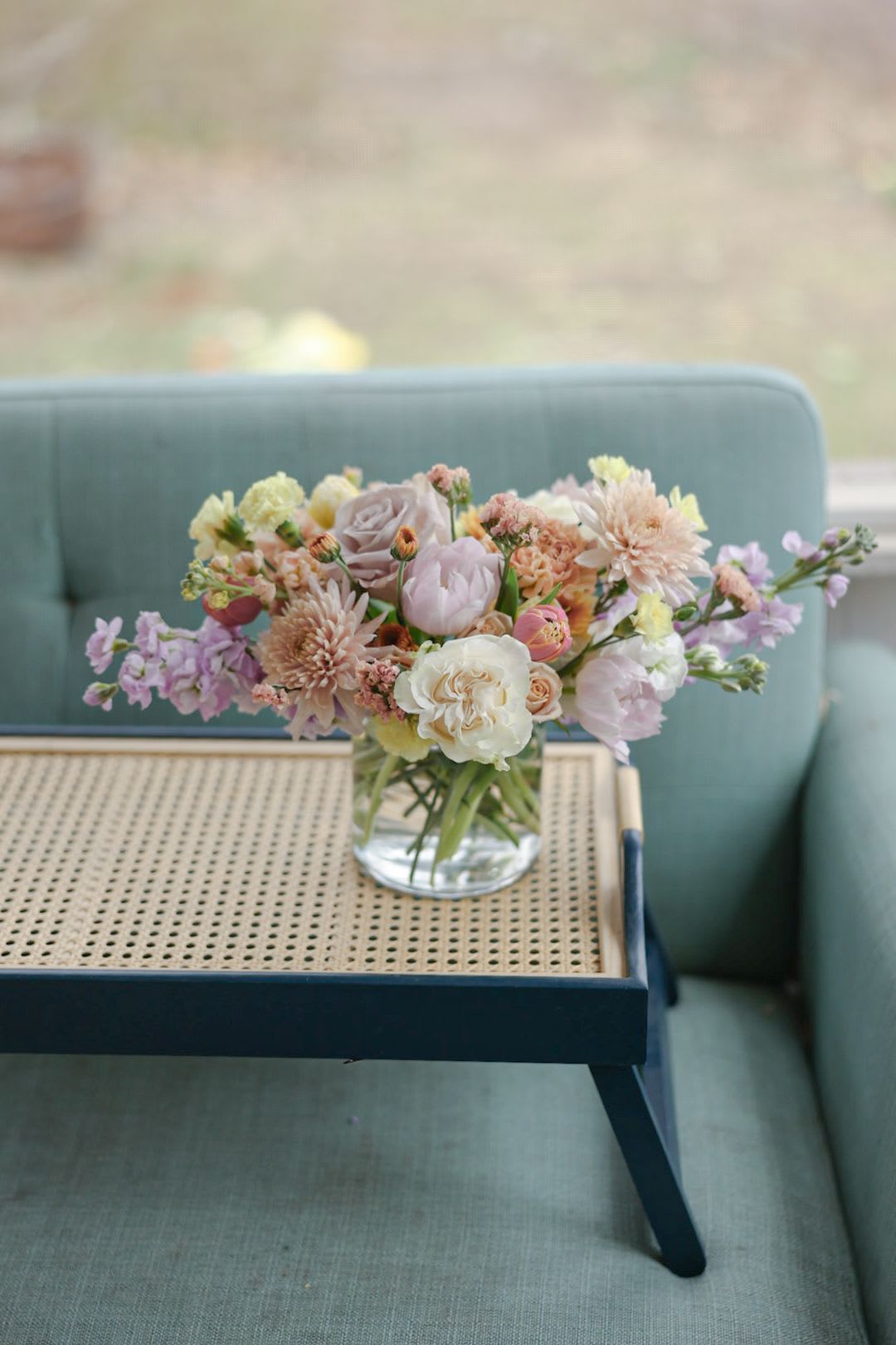 Pastel mixed flower bouquet in a clear glass vase on a tray table