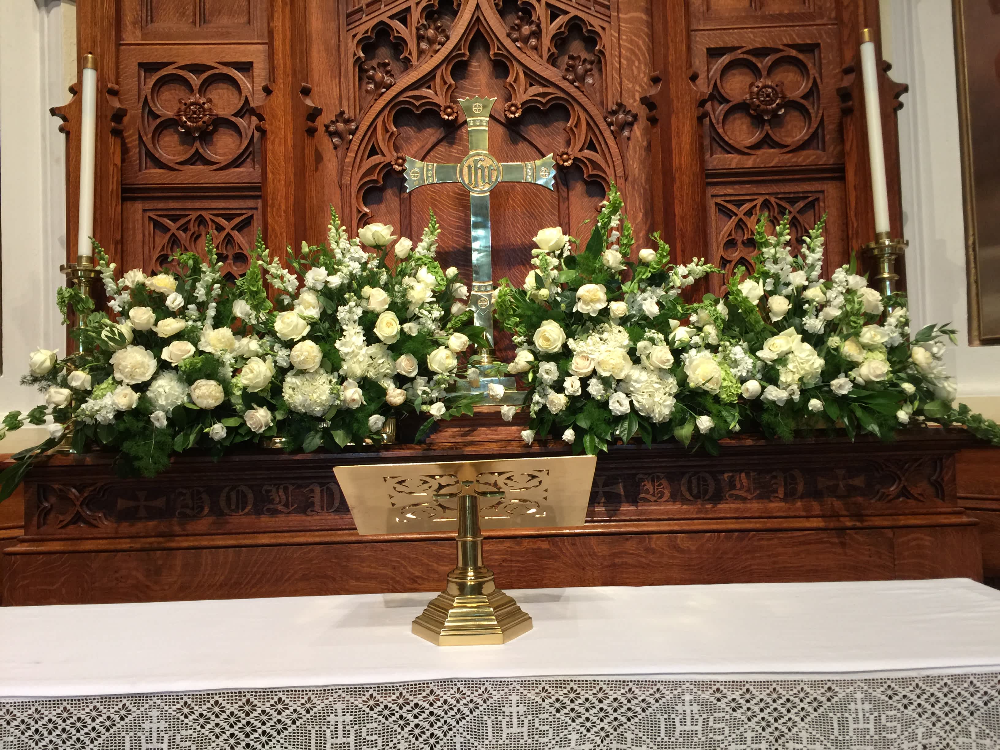 White floral arrangements flank a church altar with a cross.