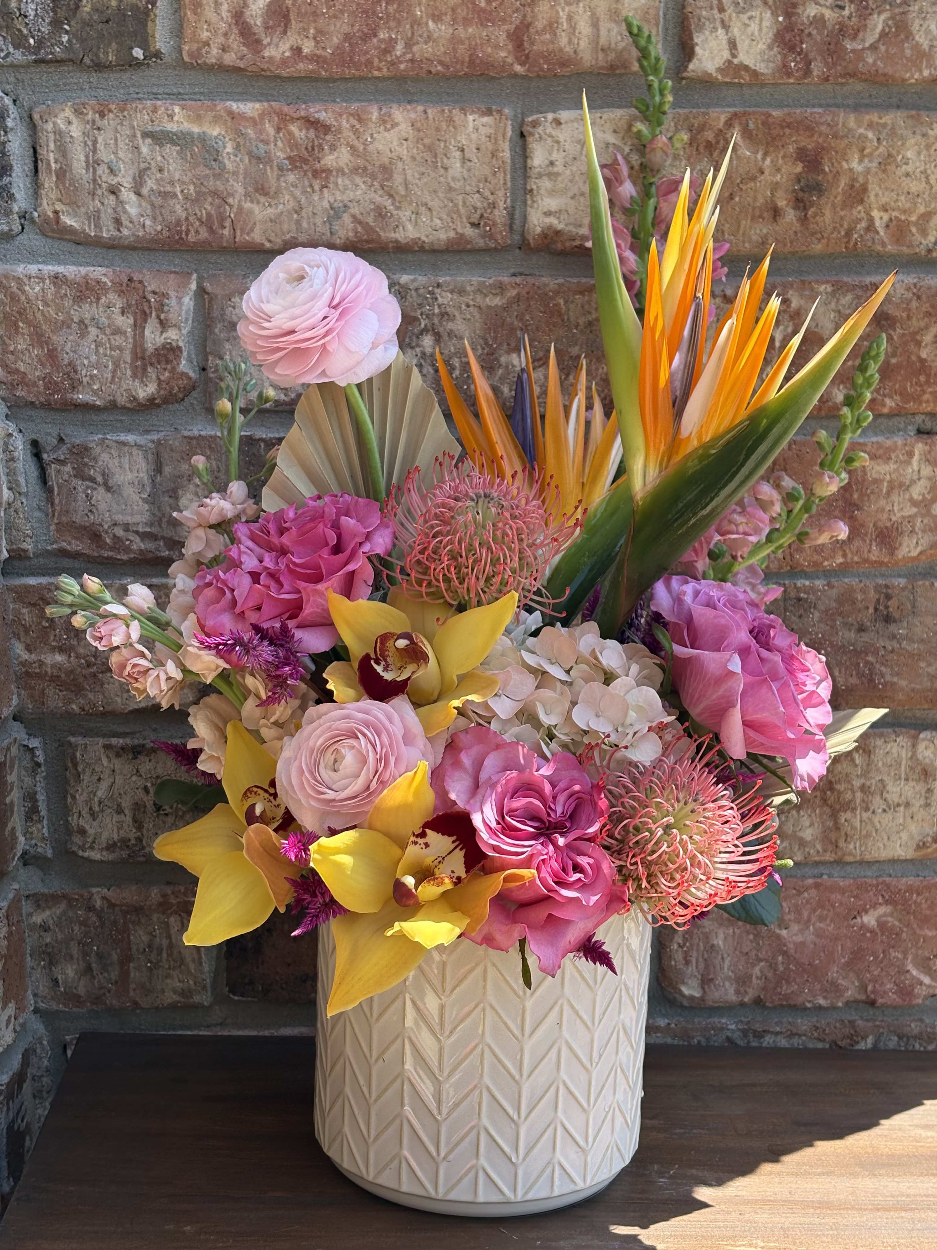 Bright tropical bouquet in a white textured vase with pink and yellow blooms