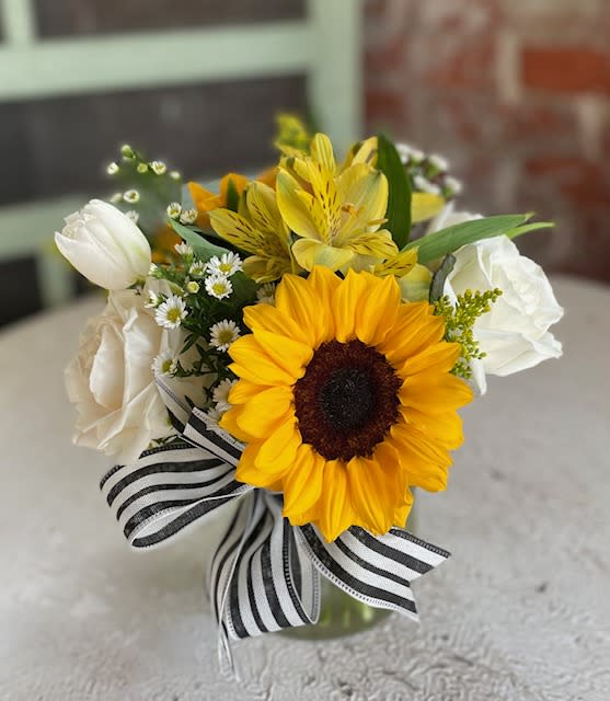 Sunflower bouquet with white tulips and a black-and-white striped ribbon in a glass vase