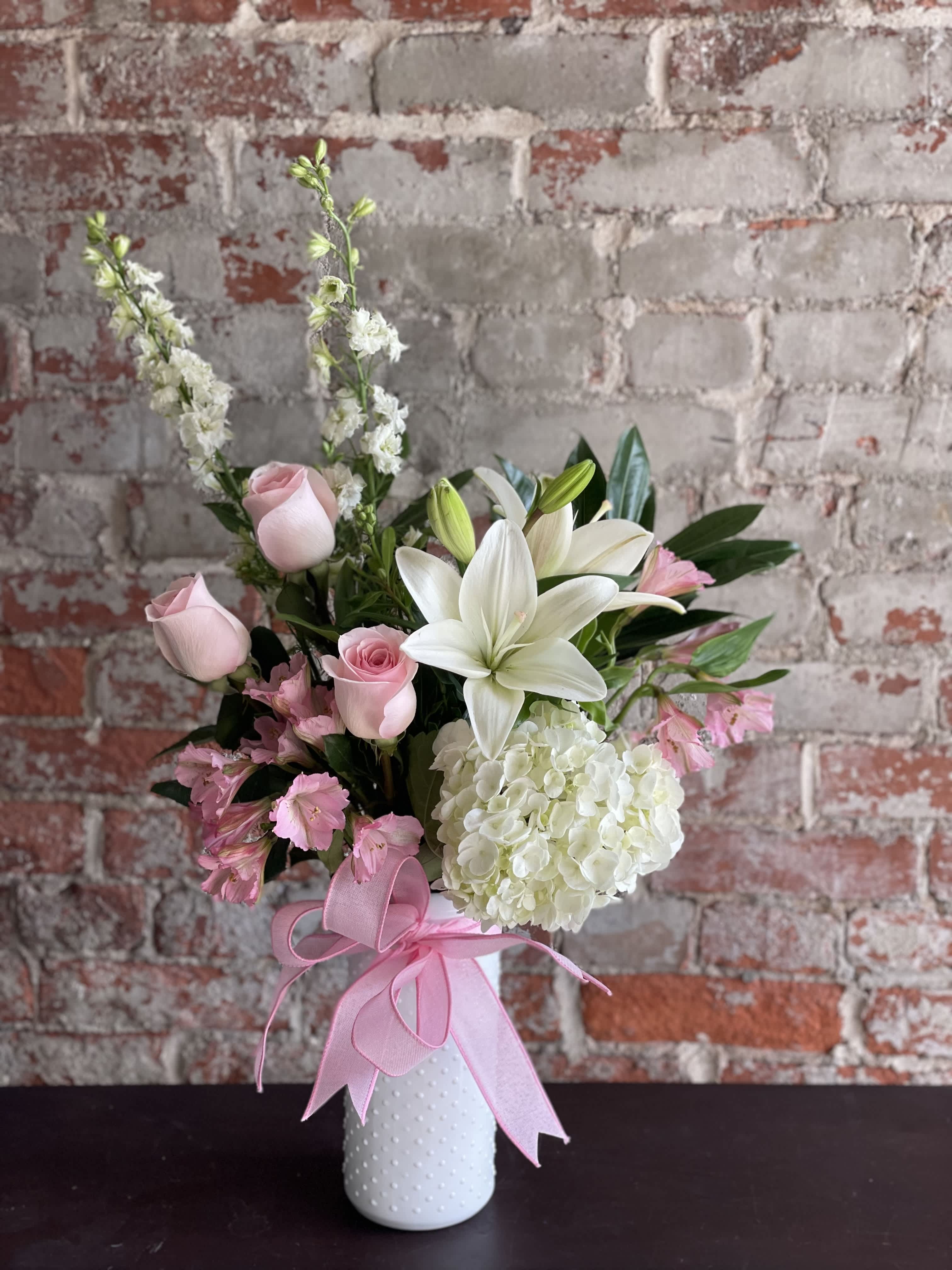 Pink roses and white lilies in a white vase with a pink ribbon