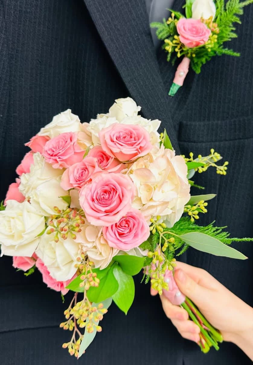 Pink and white rose bouquet with greenery, plus a matching boutonniere on a dark suit