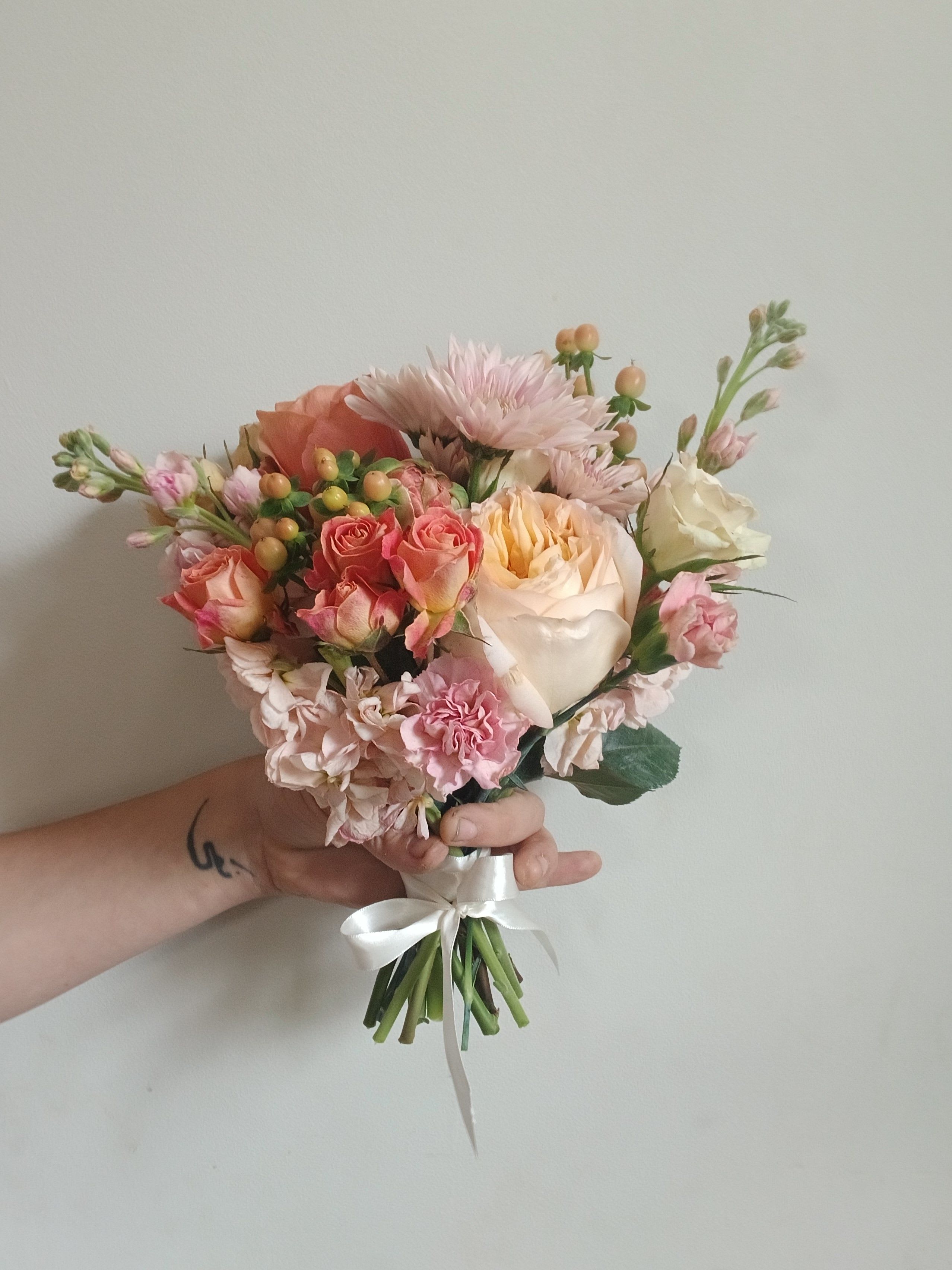 Handheld bouquet of pink and cream roses with pale blooms and a white ribbon