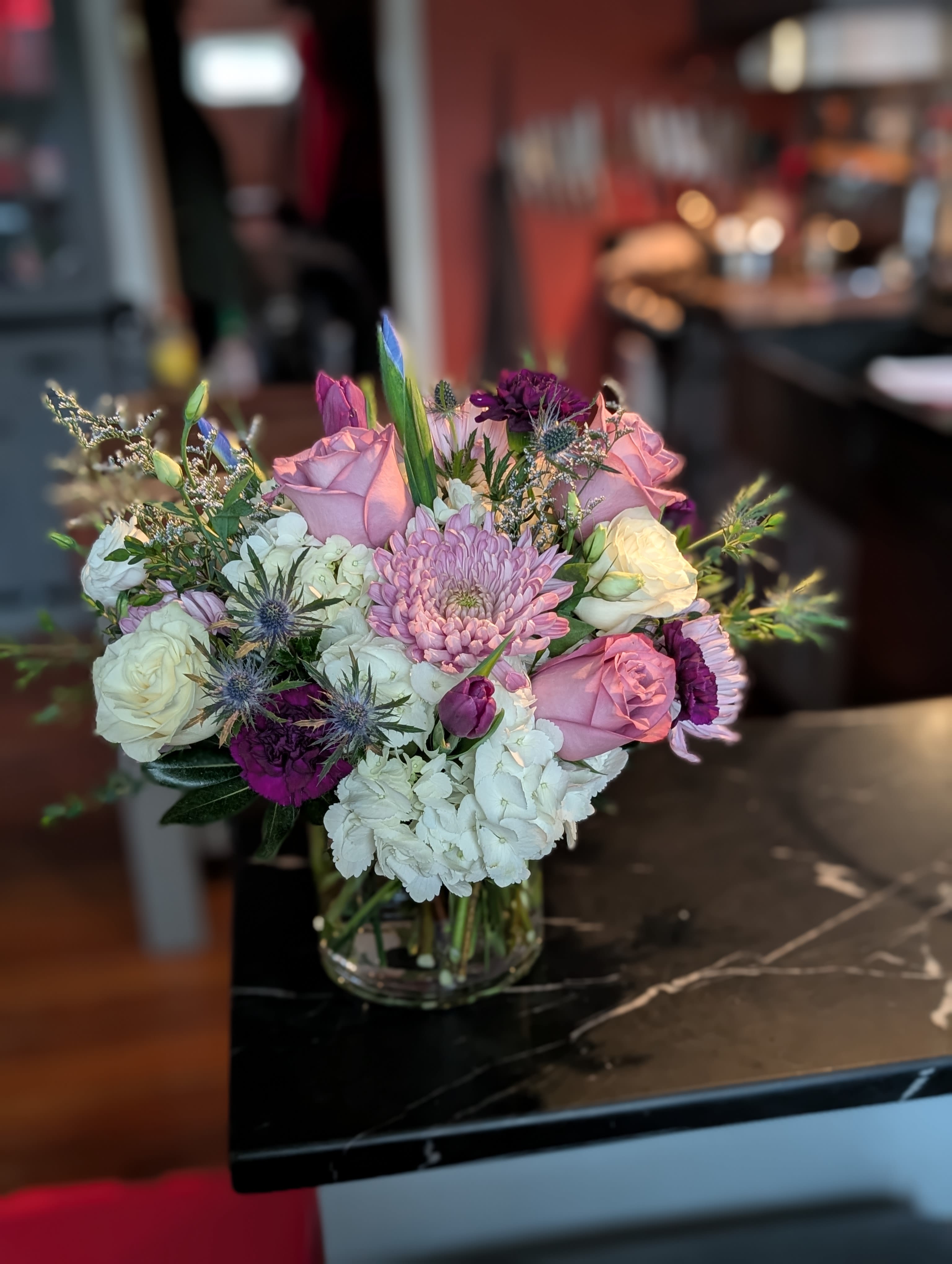 Lavender Luxe - A classy glass cylindrical style arrangement in shades of lavender, indigo, royal purple and whites is sure to delight the senses. Fragrant roses, full hydrangeas, plentiful cremons and plum carnations are just a few selections featured in the photo. We will do the best to match the photo, our inventory of these colors is always shifting. Arrangement photographed is created in a 6x6in cylinder vase. Created by Kate.