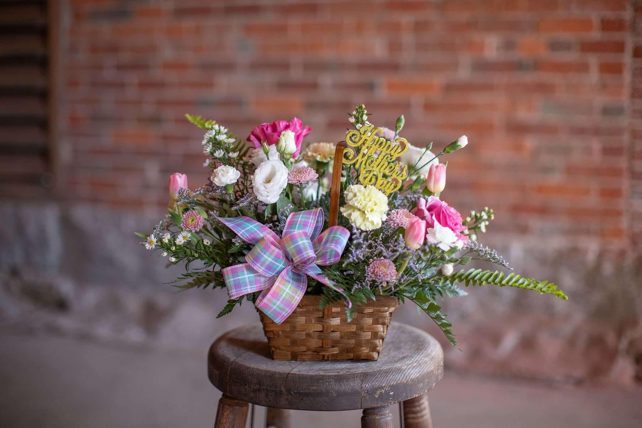 Premium HMD Basket - A florist's fresh assortment of hand-selected blooms in pastel shades in a wicker basket. The floral arrangement is finished with a festive bow and shimmering "Happy Mother's Day," wood pick in pink, yellow, or lavender colors. Standard is for a 6-7 inch wicker basket. Upgrading to deluxe will be an 8 inch whitewash basket. Premium will be in a 9 inch willow basket.