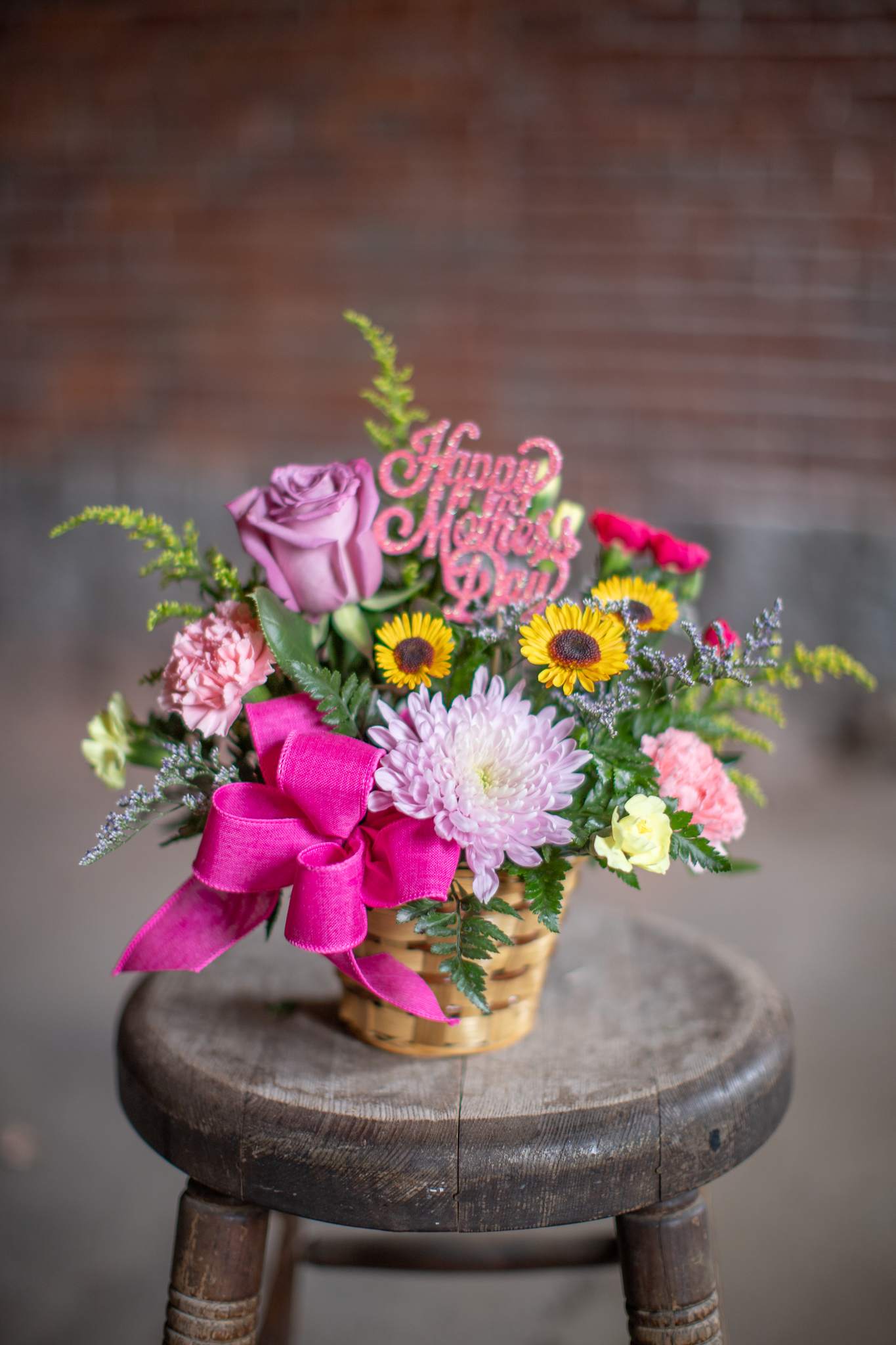 Happy Mother's Day Basket - A colorful basket of fresh flowers arranged around an iridescent decorative greeting pick. "happy Mother's Day picks come in assorted colors. The flower varieties will compliment the carved wooden greeting pick. A very cute arrangement expresses the love, gratitude and admiration we have for everything our mom's do for us. 