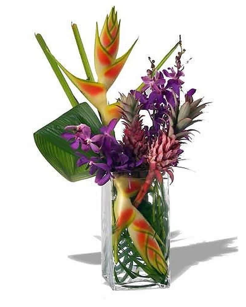 Tropical arrangement with orange and yellow blooms and purple orchids in a clear glass vase