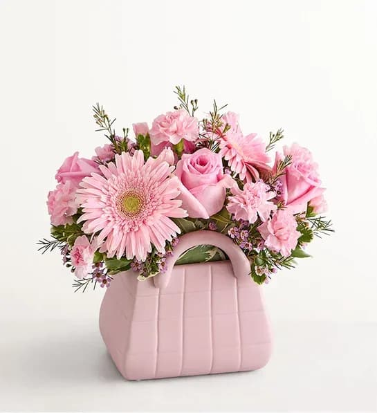 Designer Dream Bouquet - Arrangement of pink roses, Gerbera daisies, mini carnations, and waxflowers accented with assorted greenery Artistically designed in a keepsake pink vase designed to resemble a handbag; measures 6.3”H